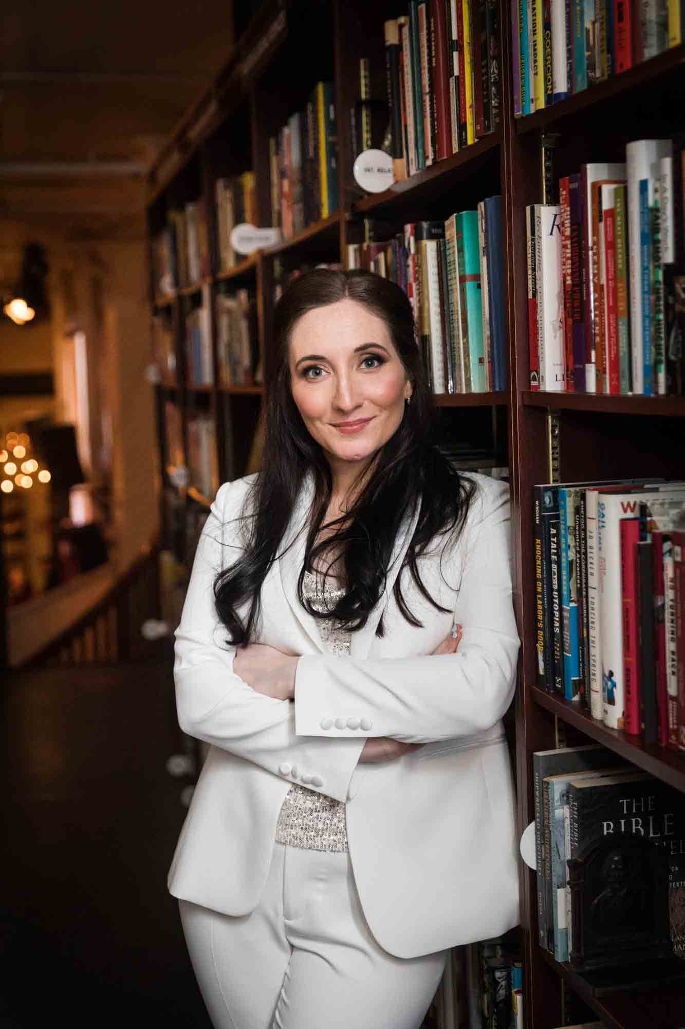 Bride in white tuxedo in front of bookcase at a Housing Works Bookstore wedding