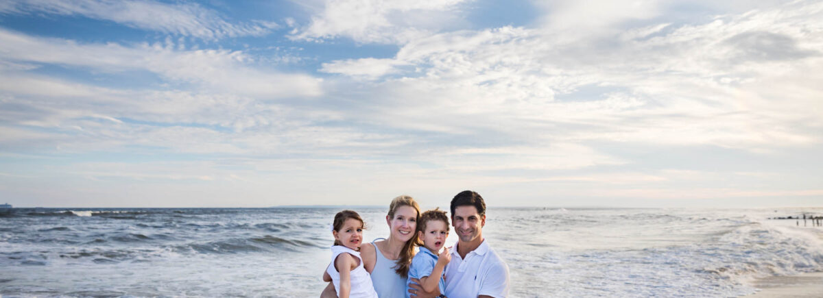 Family standing on beach in front of ocean for an article on beach family portrait tips
