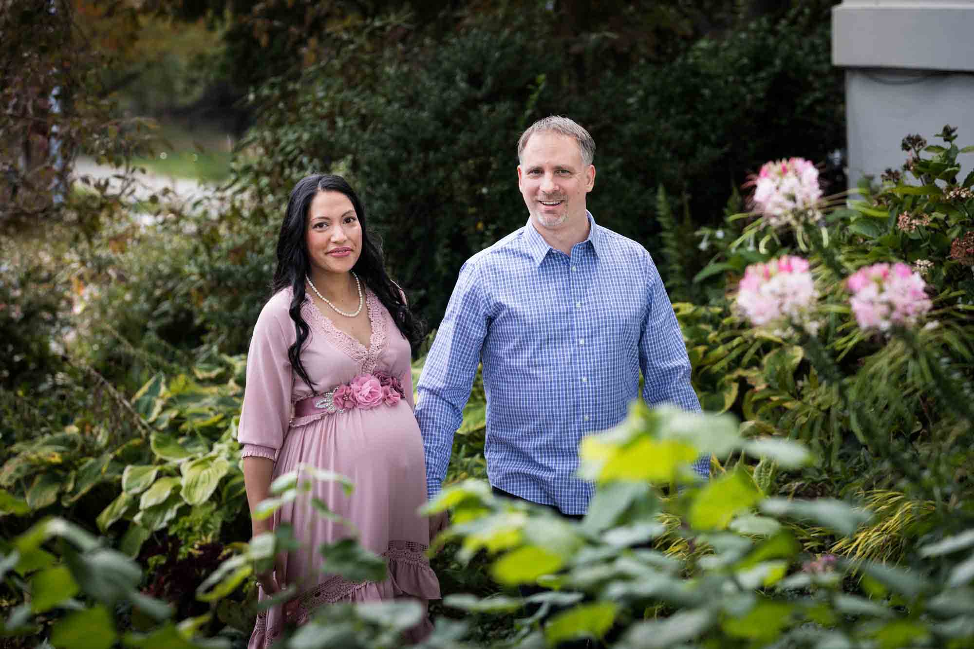 Maternity photos of couple walking in front of flowers in Forest Park