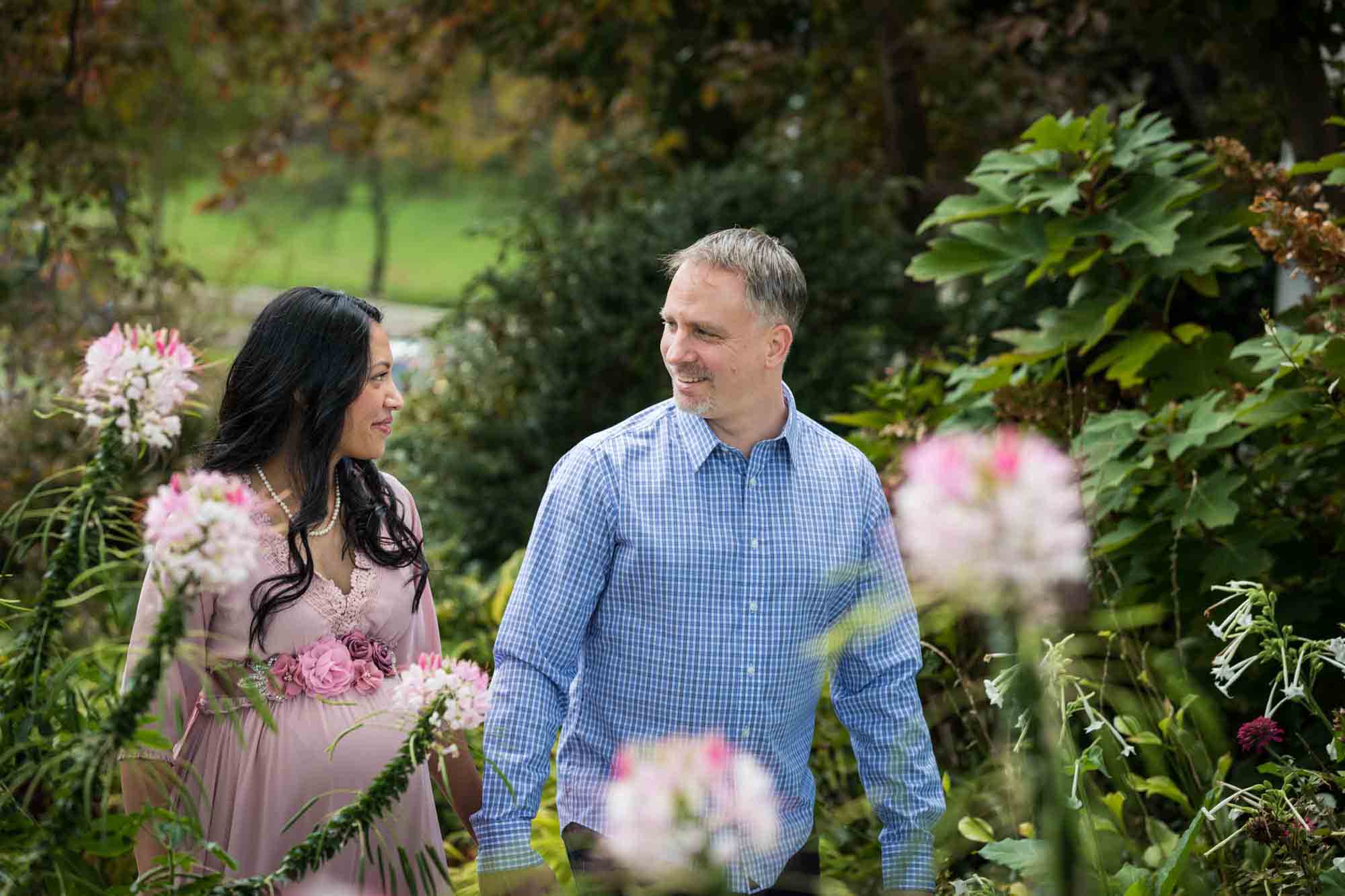 Maternity photos of couple walking in front of flowers in Forest Park