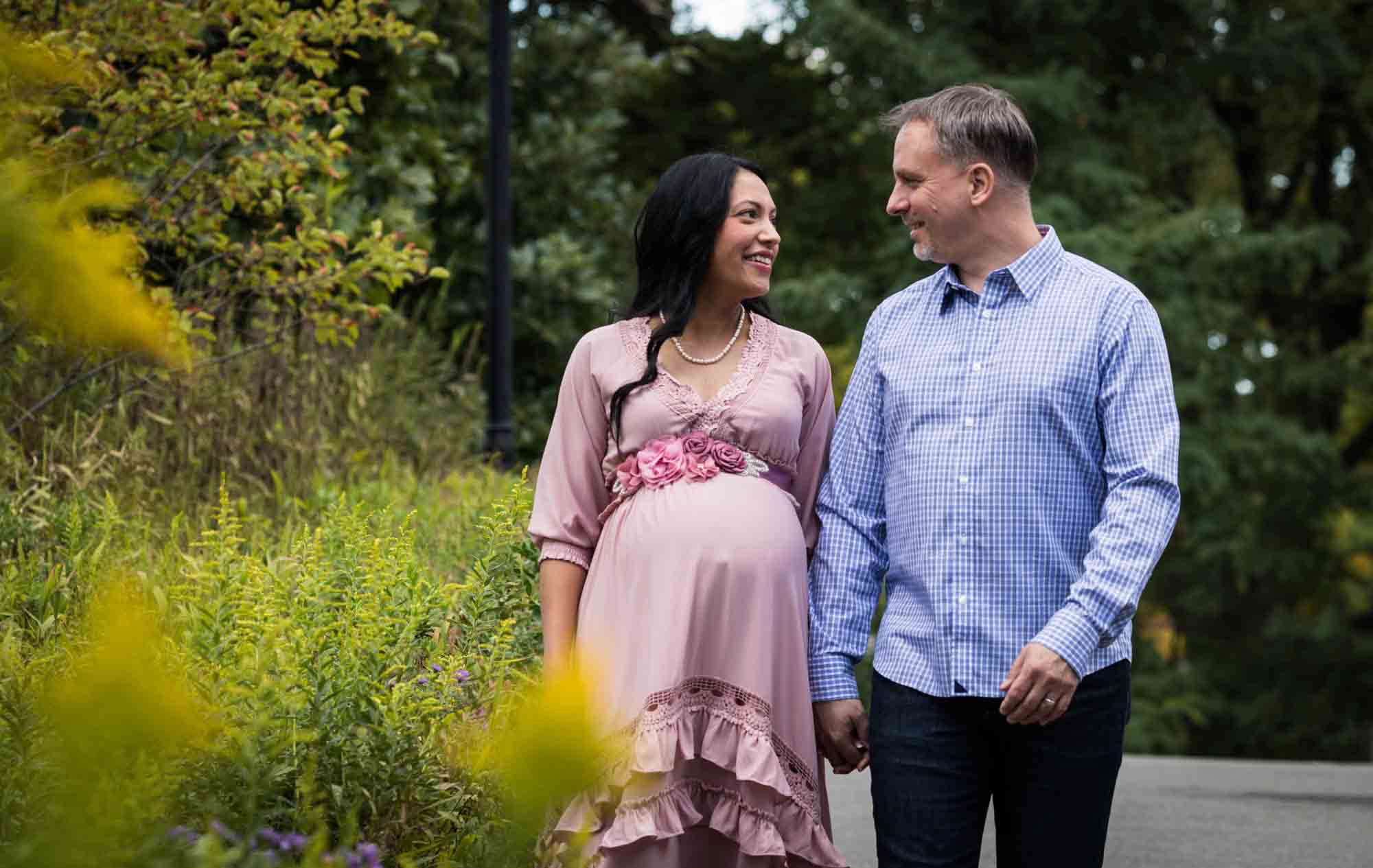 Maternity photos of couple walking in front of flowers in Forest Park