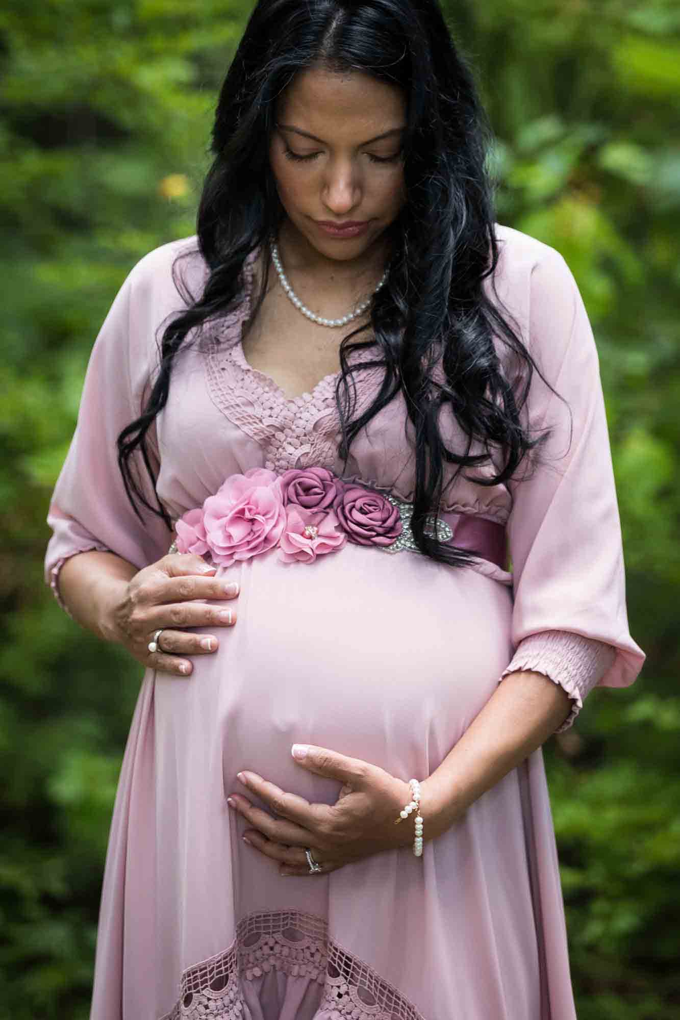 Forest Park maternity photos of a woman with brown hair wearing a pink dress in a forest