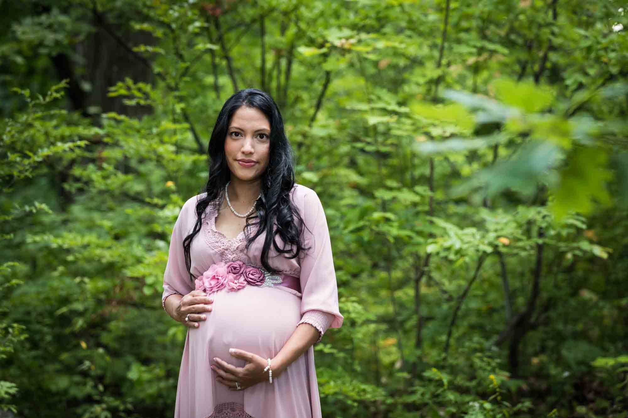Forest Park maternity photos of a woman with brown hair wearing a pink dress in a forest