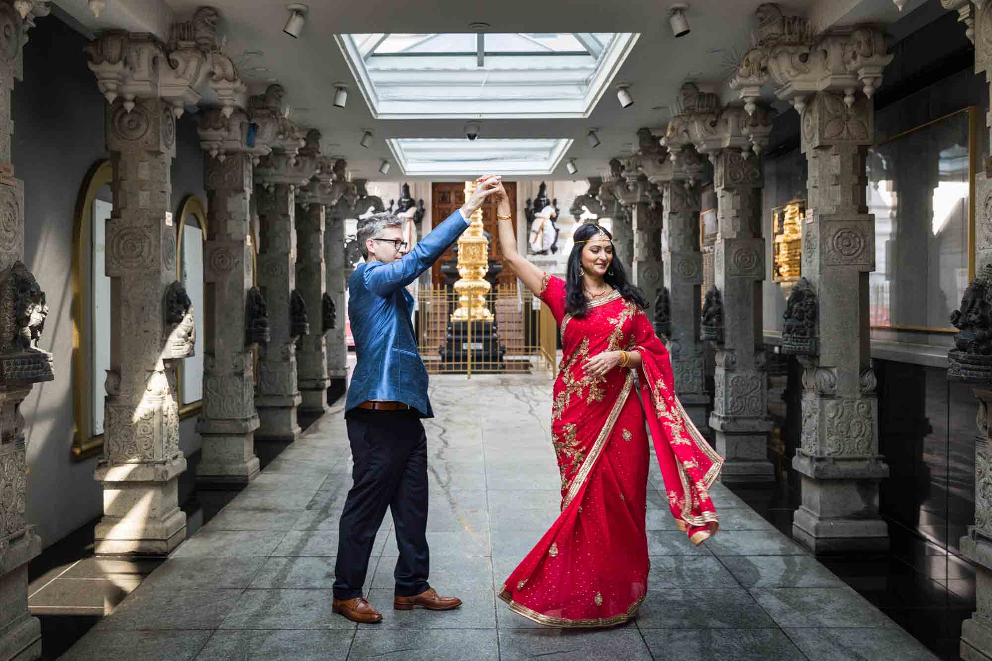Hindu Temple Society of North America wedding photos of groom in blue jacket twirling bride wearing red sari