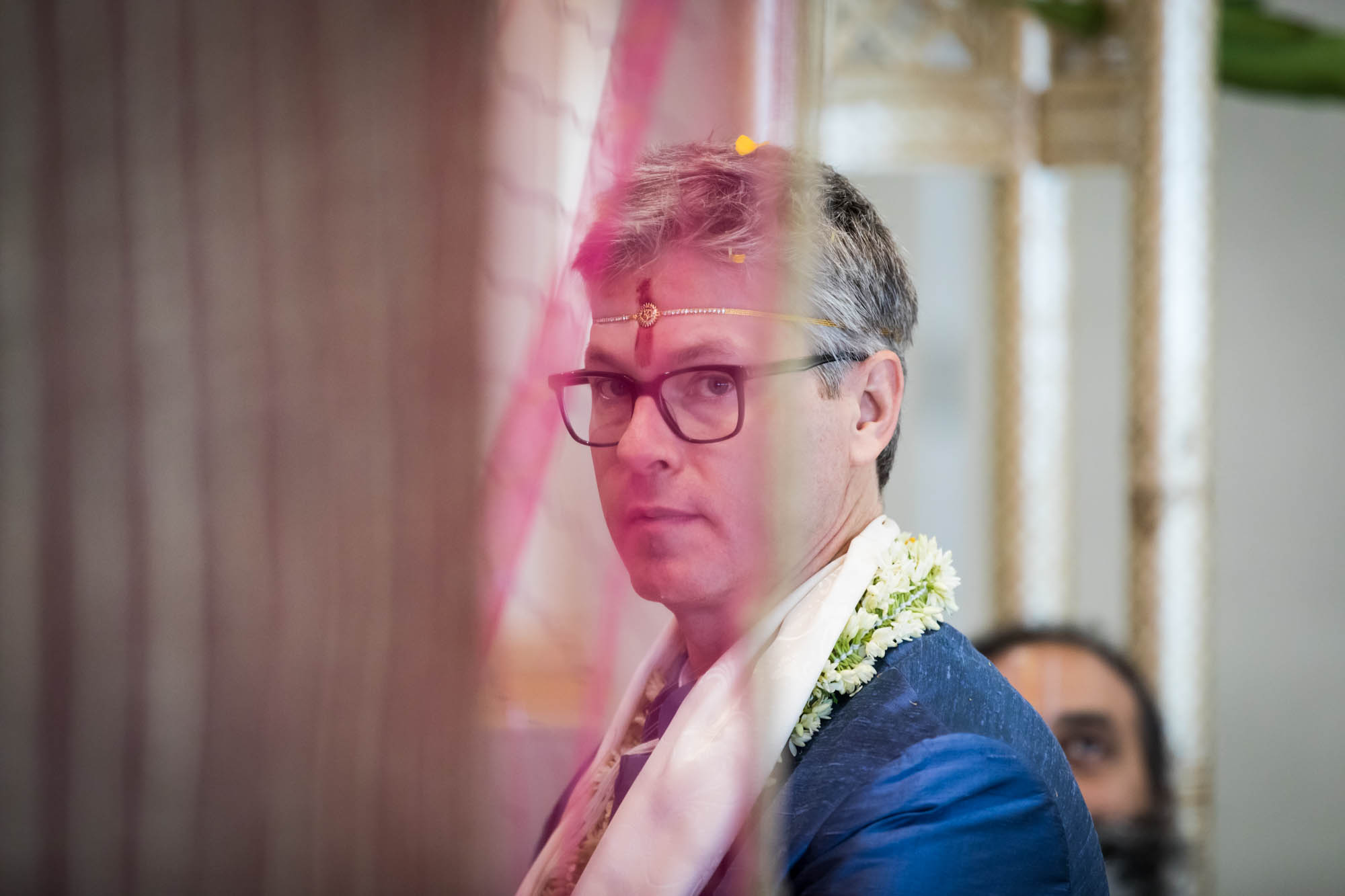 Flushing Temple wedding photos of groom wearing blue jacket behind pink curtain