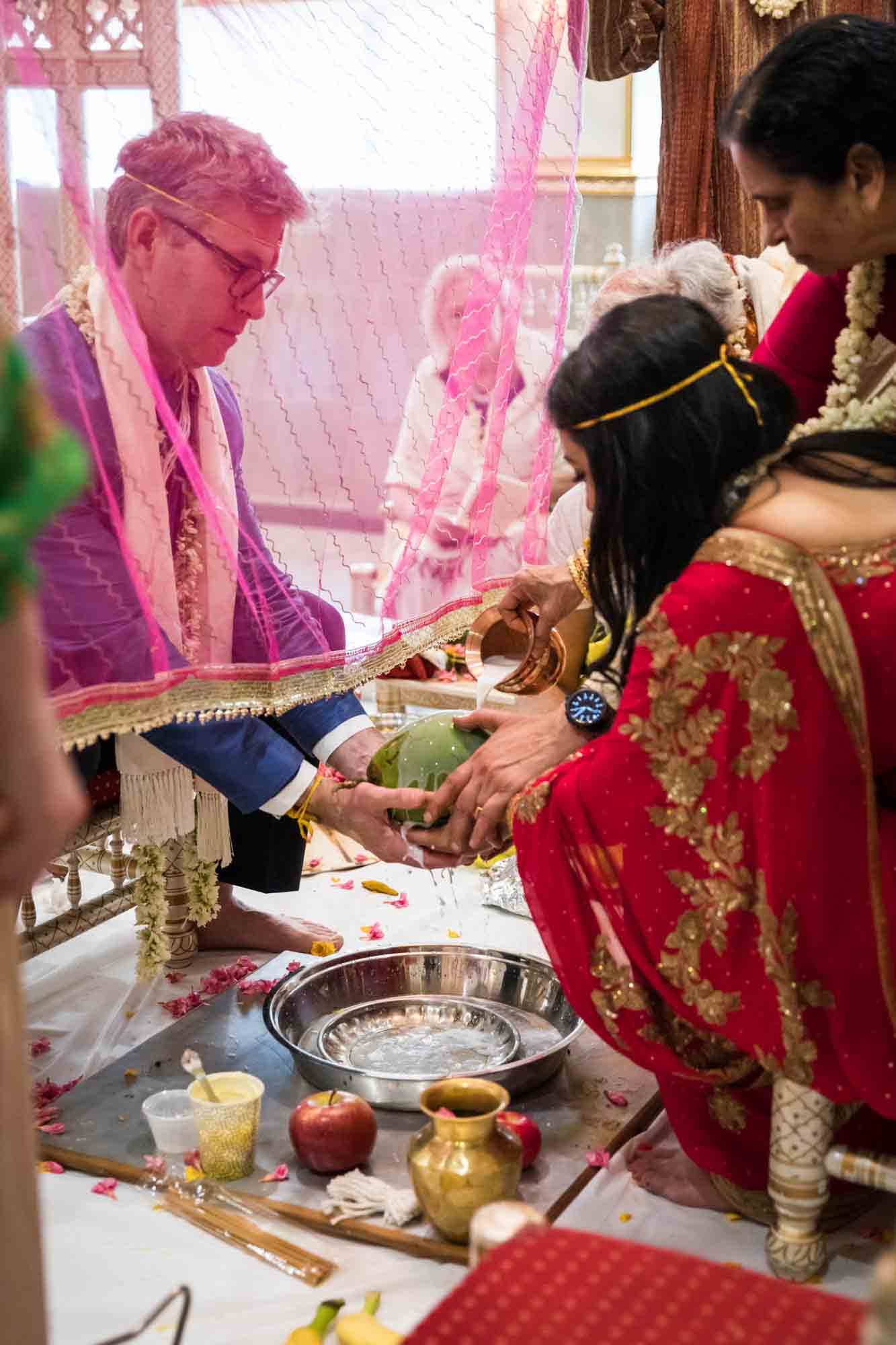 Bride and groom holding coconut under pink curtain at a Hindu Temple Society of North America wedding