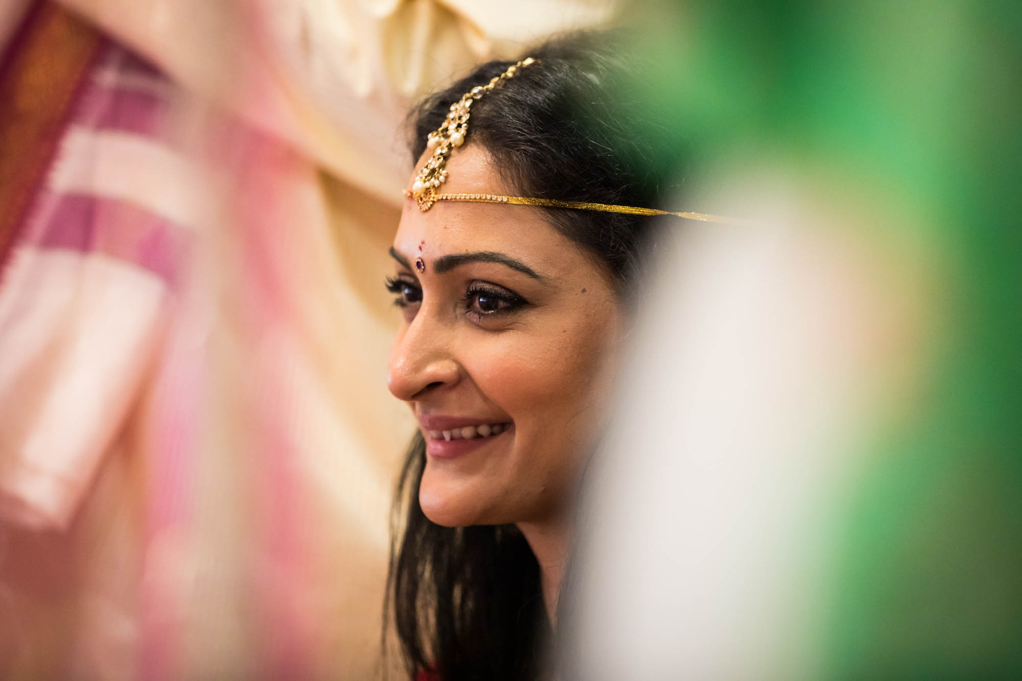Smiling bride with gold jewelry on her head at a Hindu Temple Society of North America wedding