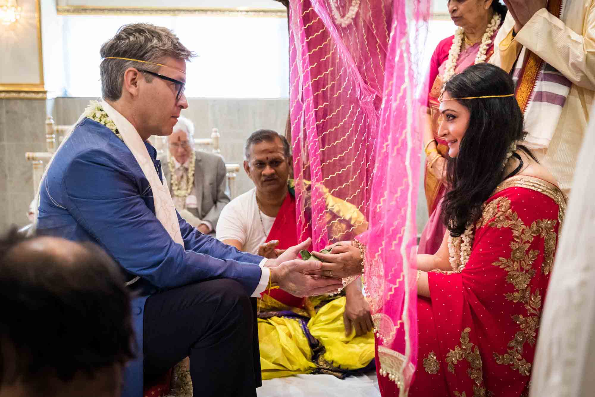 Bride and groom looking at each other under pink curtain at a Hindu Temple Society of North America wedding