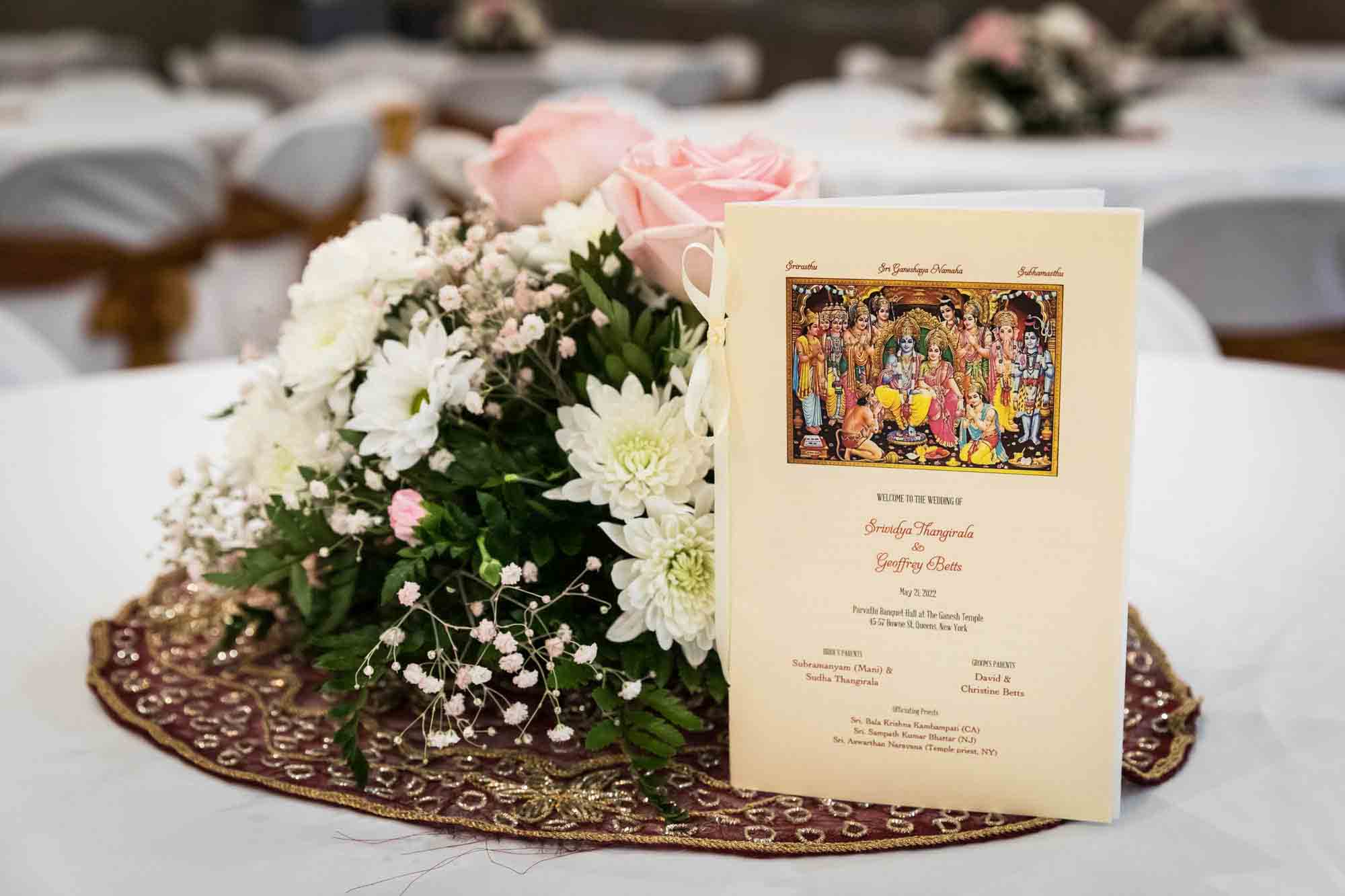 Vedic ceremony program beside bouquet of flowers on a table
