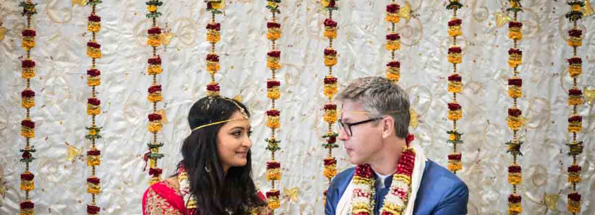 Hindu Temple Society of North America wedding photos of bride and groom holding hands against a white backdrop with flower garlands
