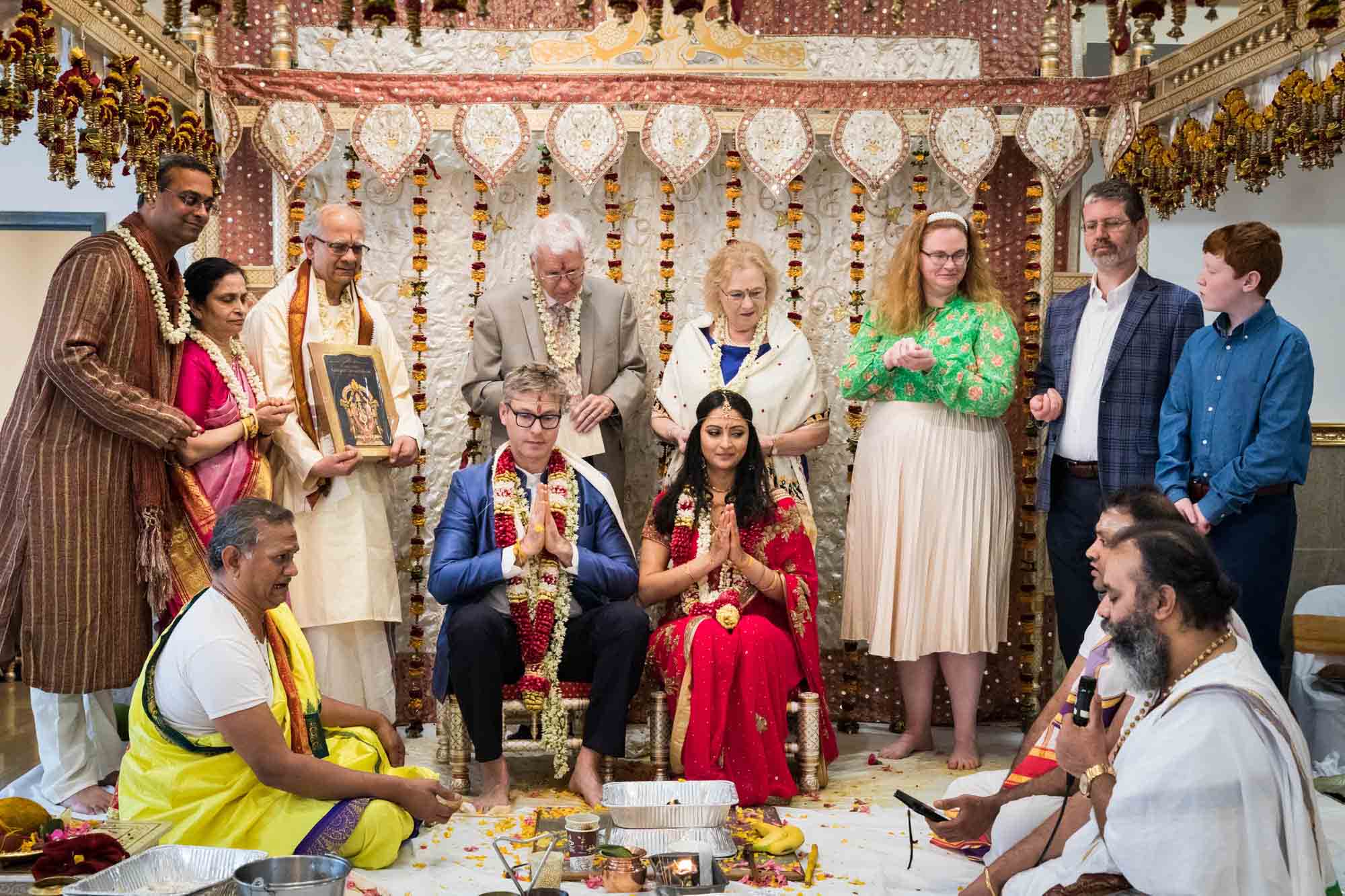 Bride and groom with folded hands praying with family and priests at a Ganesha Temple wedding