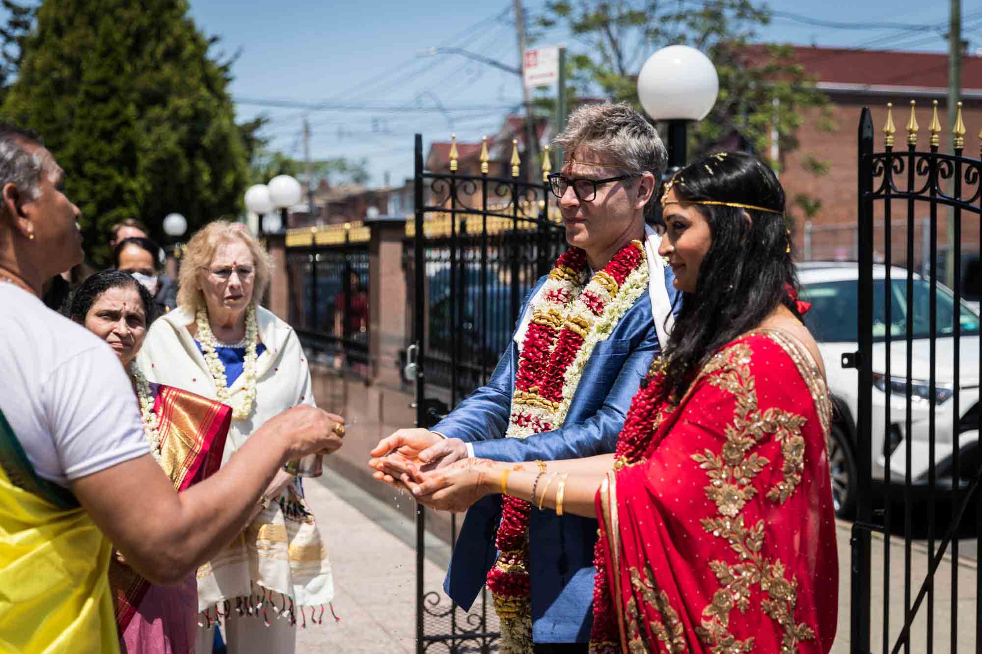 Bride and groom holding out hands to priest outdoors at a Ganesha Temple wedding