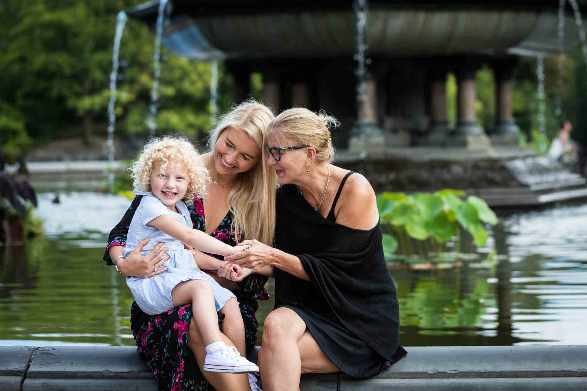 Mother and grandmother holding little blond girl at Bethesda Fountain for an article on NYC family portrait tips for tourists