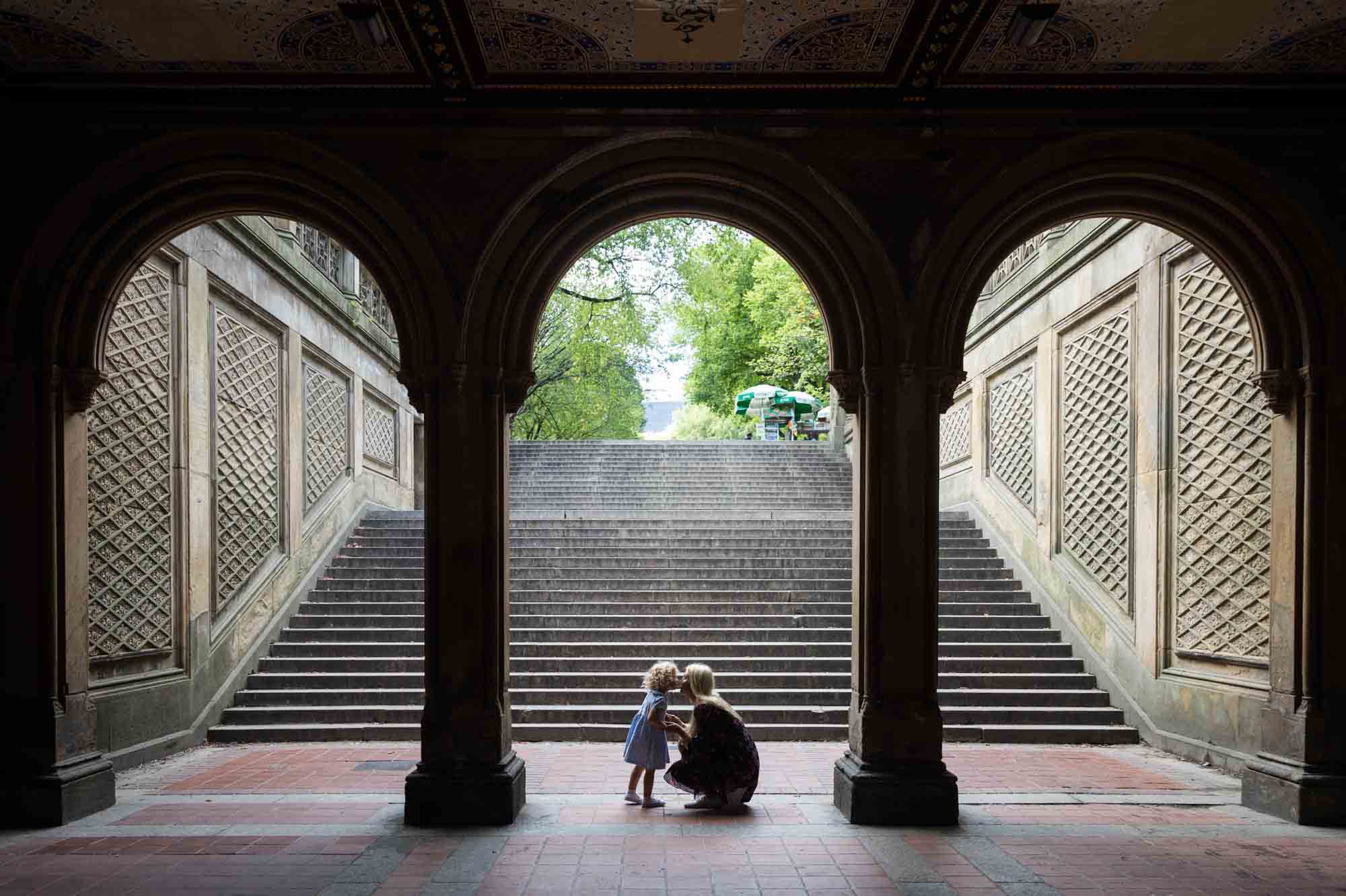 Mother and little girl kissing under arch of Bethesda Terrace for an article on NYC family portrait tips for tourists