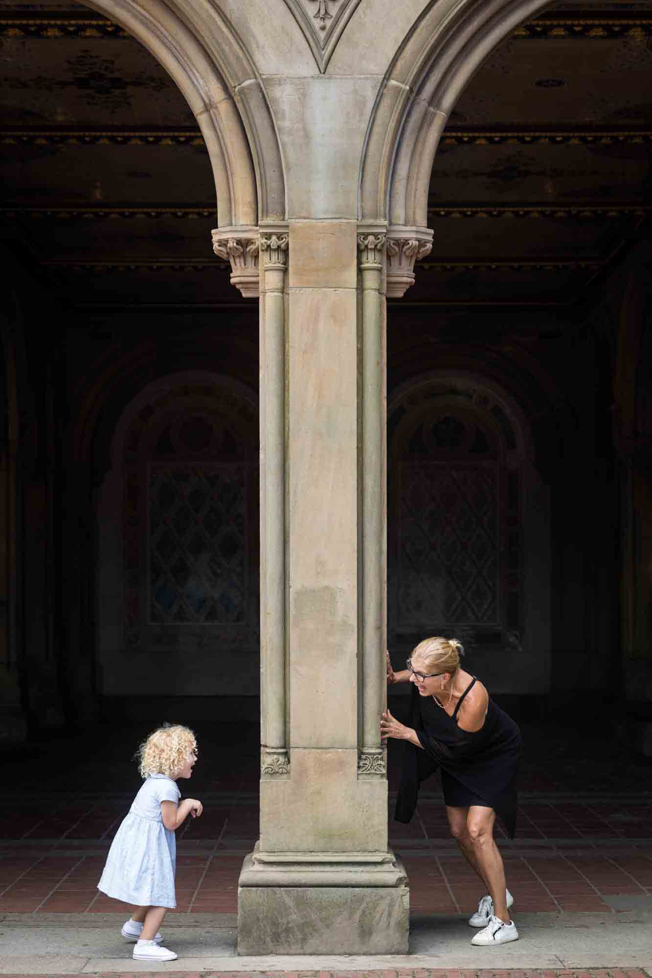 Grandmother and little girl playing around stone column for an article on NYC family portrait tips for tourists