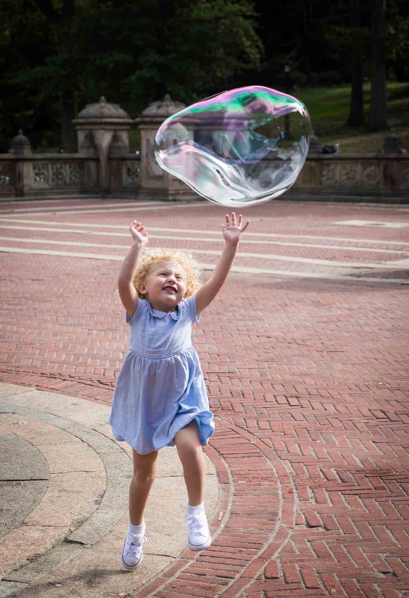Central Park family portrait of little blonde girl trying to touch giant bubble