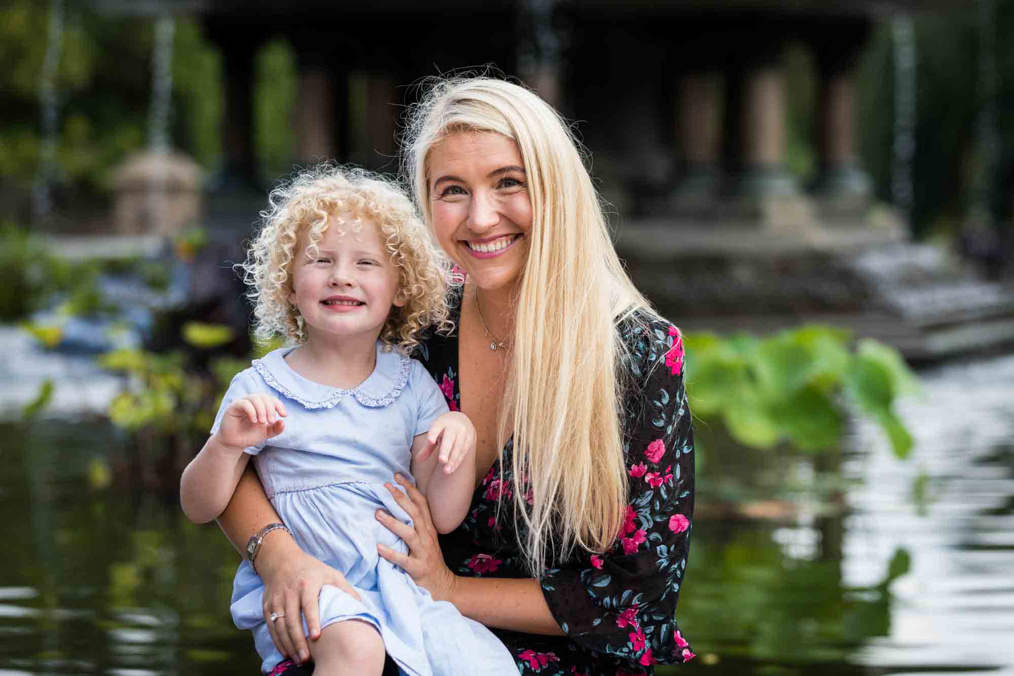 Blonde mother holding blonde girl in front of Bethesda Fountain for an article on NYC family portrait tips for tourists