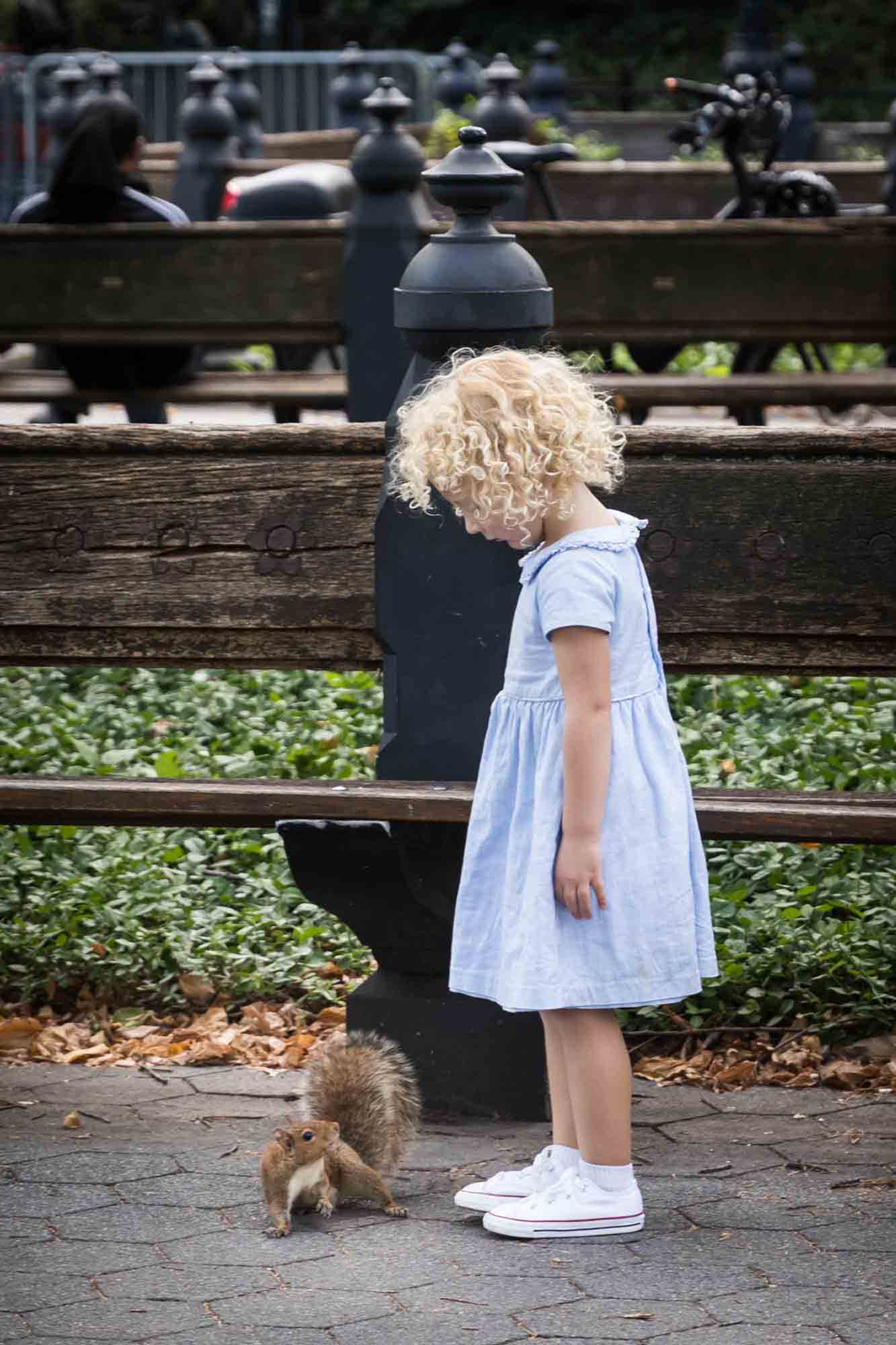 Central Park family portrait of little blonde girl looking down at squirrel