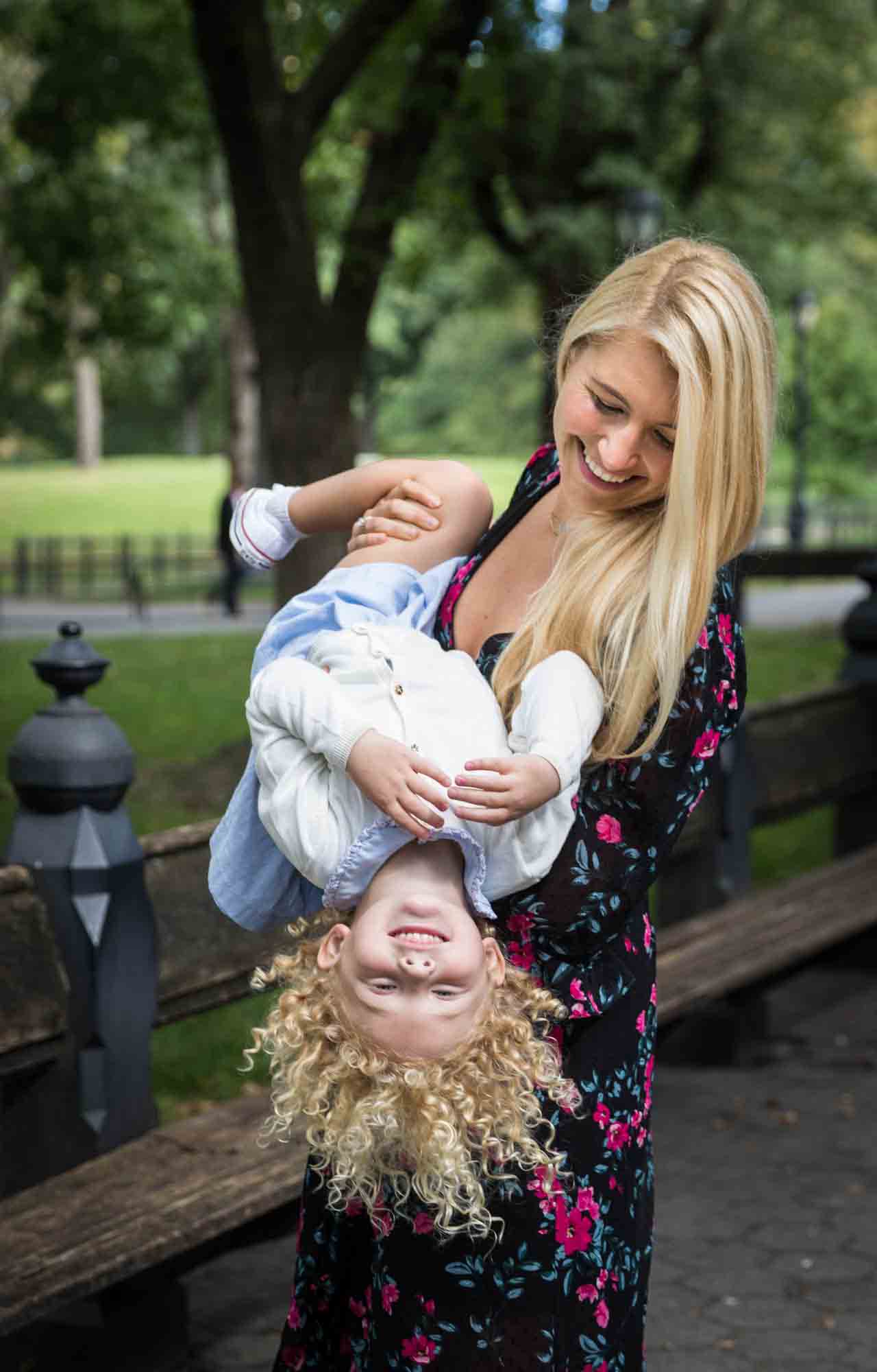 Central Park family portrait of blonde mother holding blonde little girl upside down