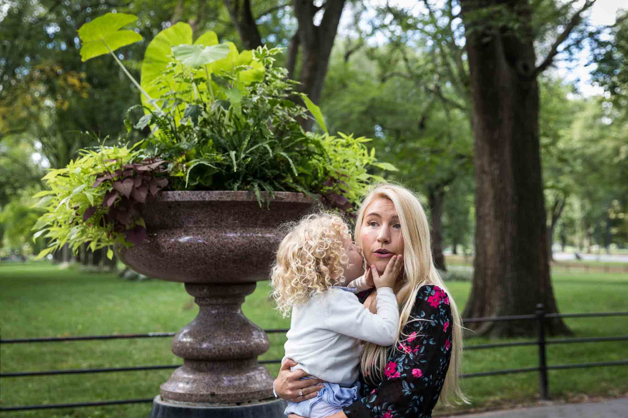 Central Park family portrait of little blonde girl kissing mother on the cheek