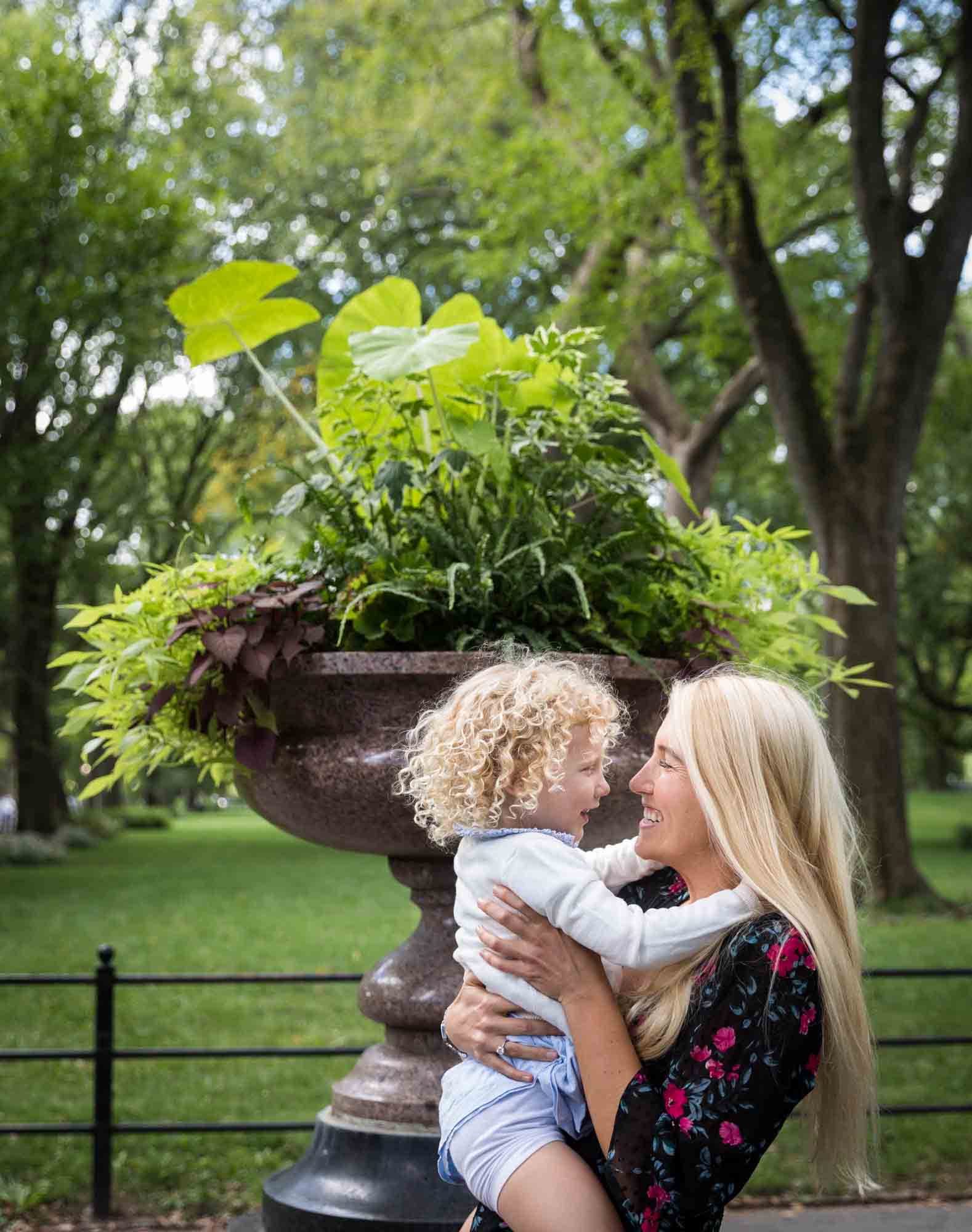 Central Park family portrait of little blonde girl touching face of mother in front of planter