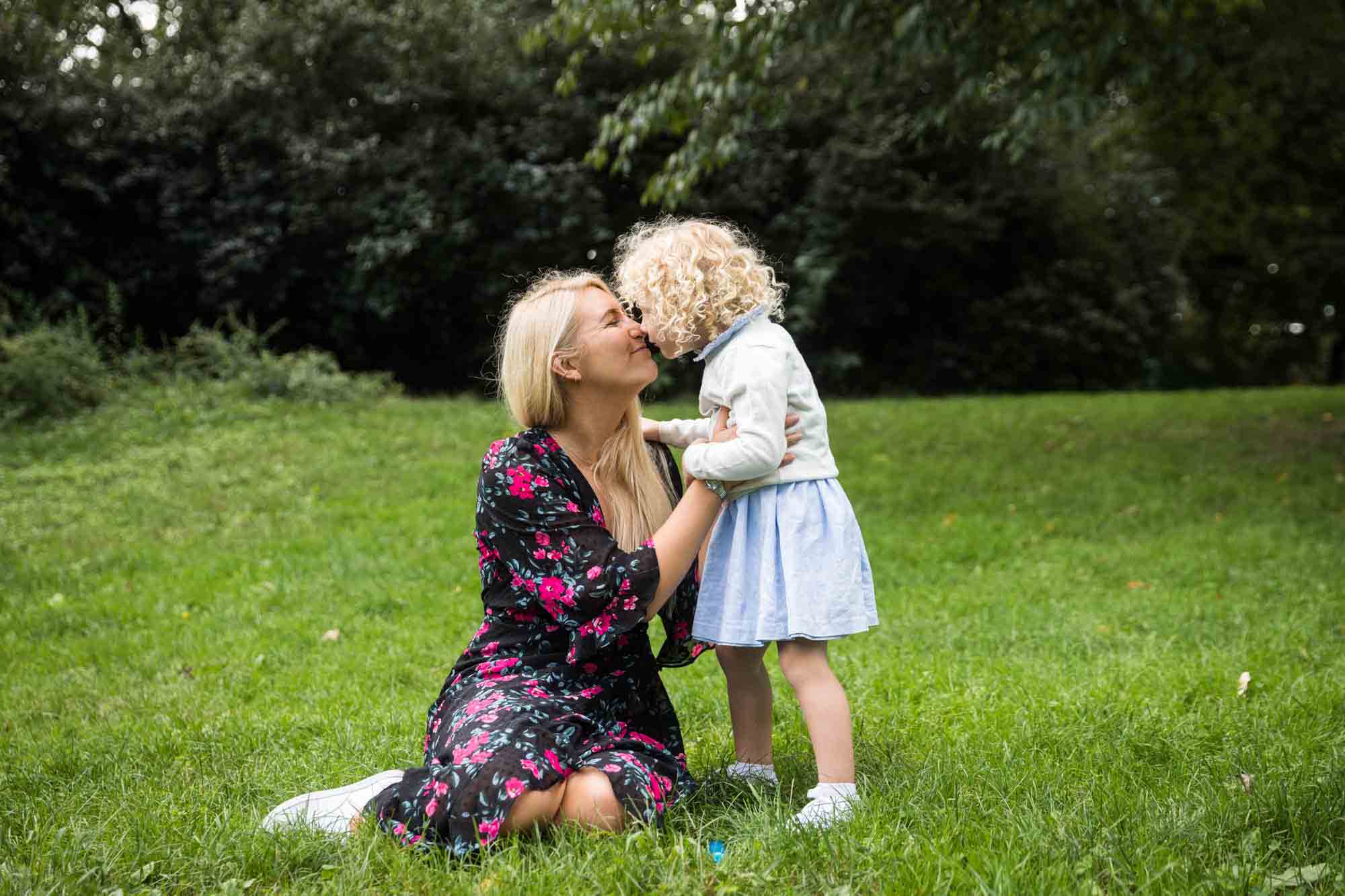Central Park family portrait of mother and little girl touching noses in grass