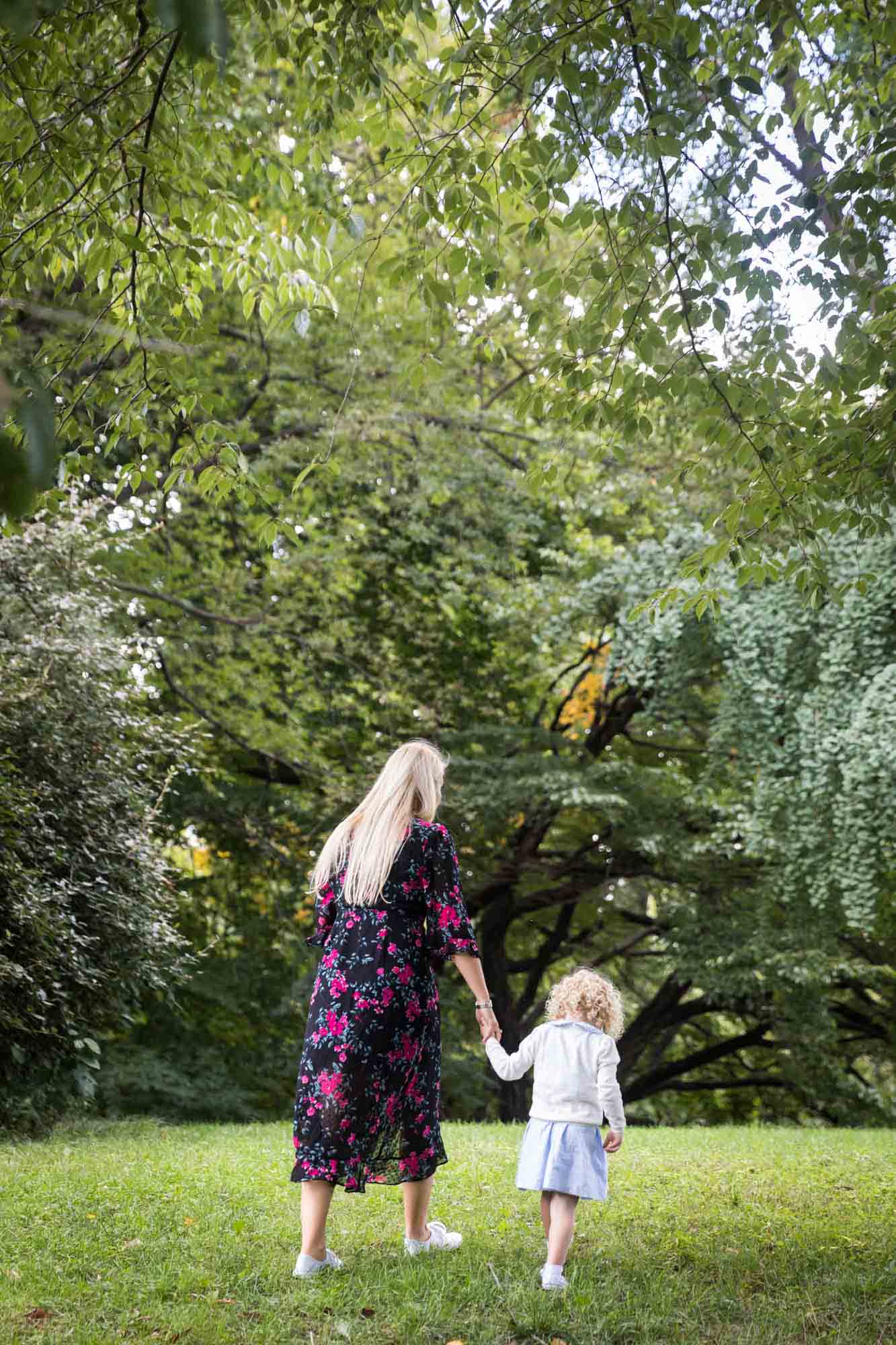 Central Park family portrait of mother and little girl holding hands and walking in forest