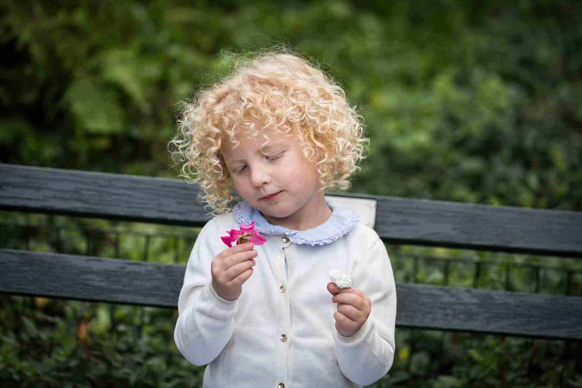 Central Park family portrait of little blonde girl looking at pink flower