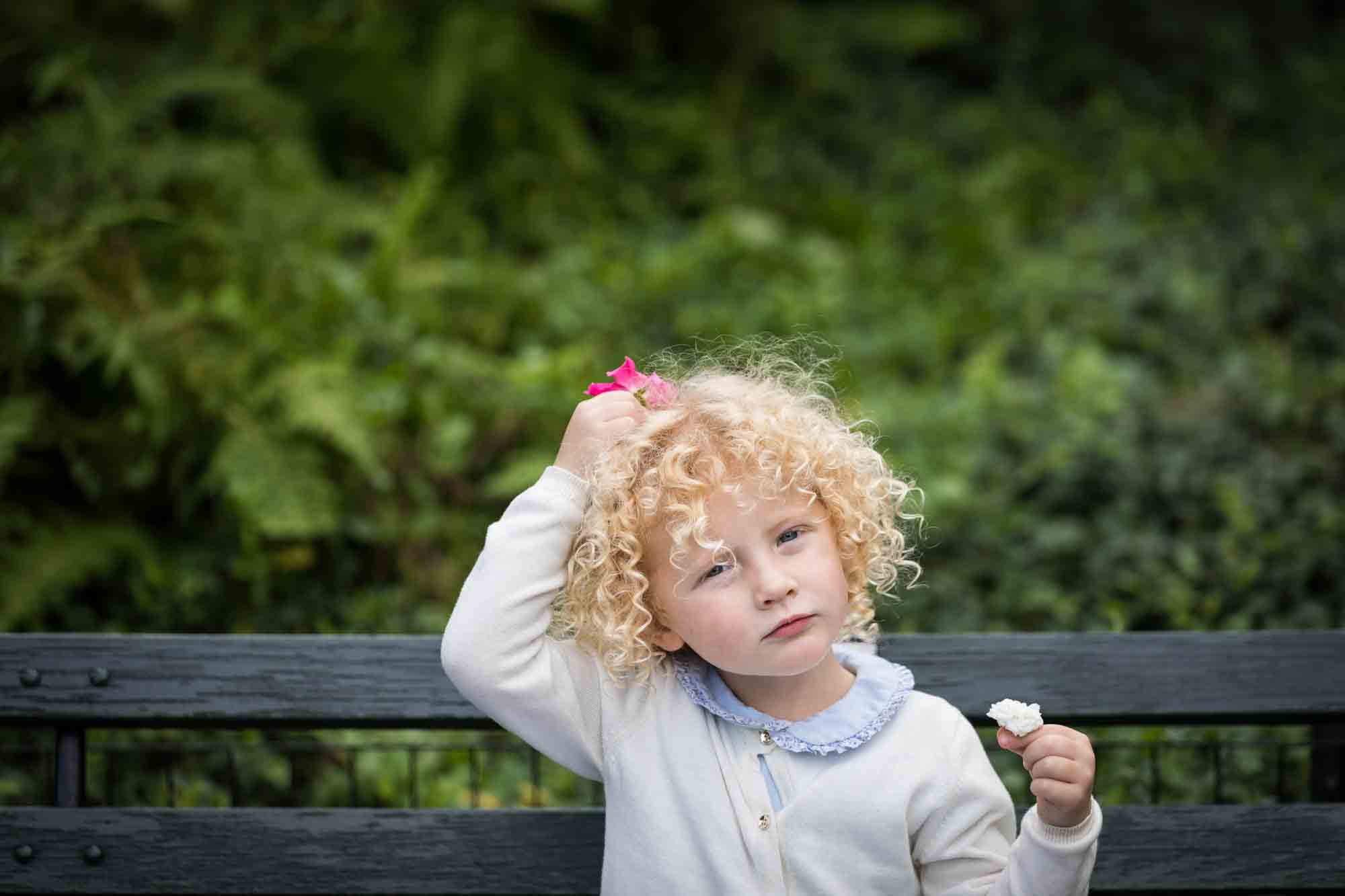 Central Park family portrait of little blonde girl holding pink flower on head