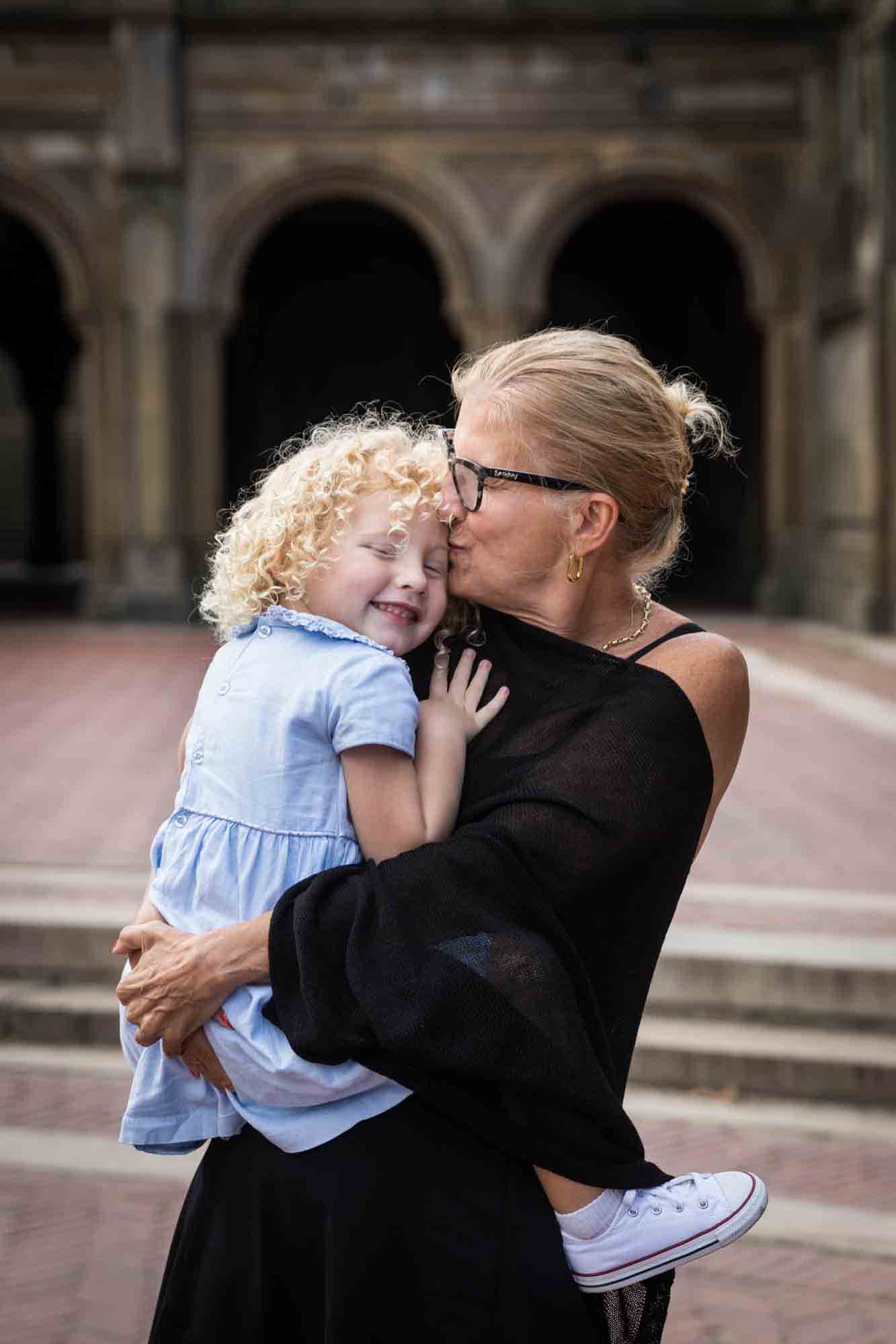 Grandmother holding little blonde girl in front of Bethesda Terrace for an article on NYC family portrait tips for tourists