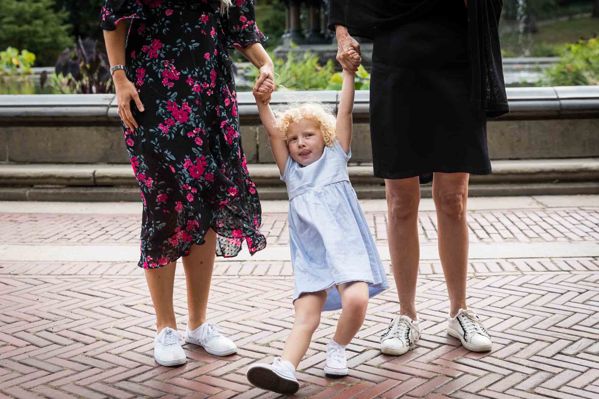 Little girl holding hands of mother and grandmother for an article on NYC family portrait tips for tourists