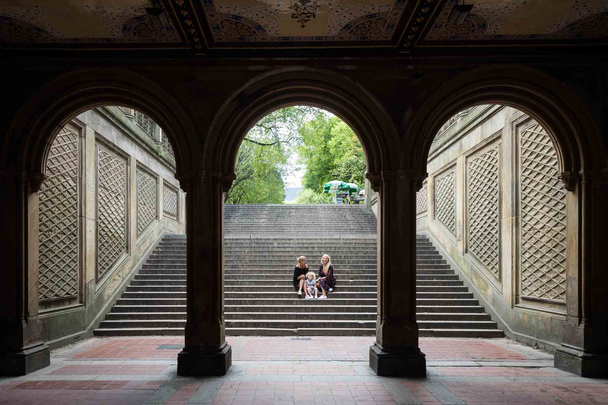 Mother, grandmother, and little girl sitting on steps in Bethesda Terrace for an article on NYC family portrait tips for tourists
