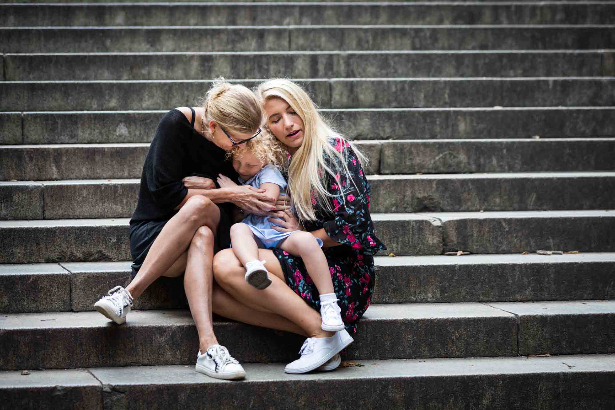 Mother, grandmother, and little girl hugging on steps for an article on NYC family portrait tips for tourists