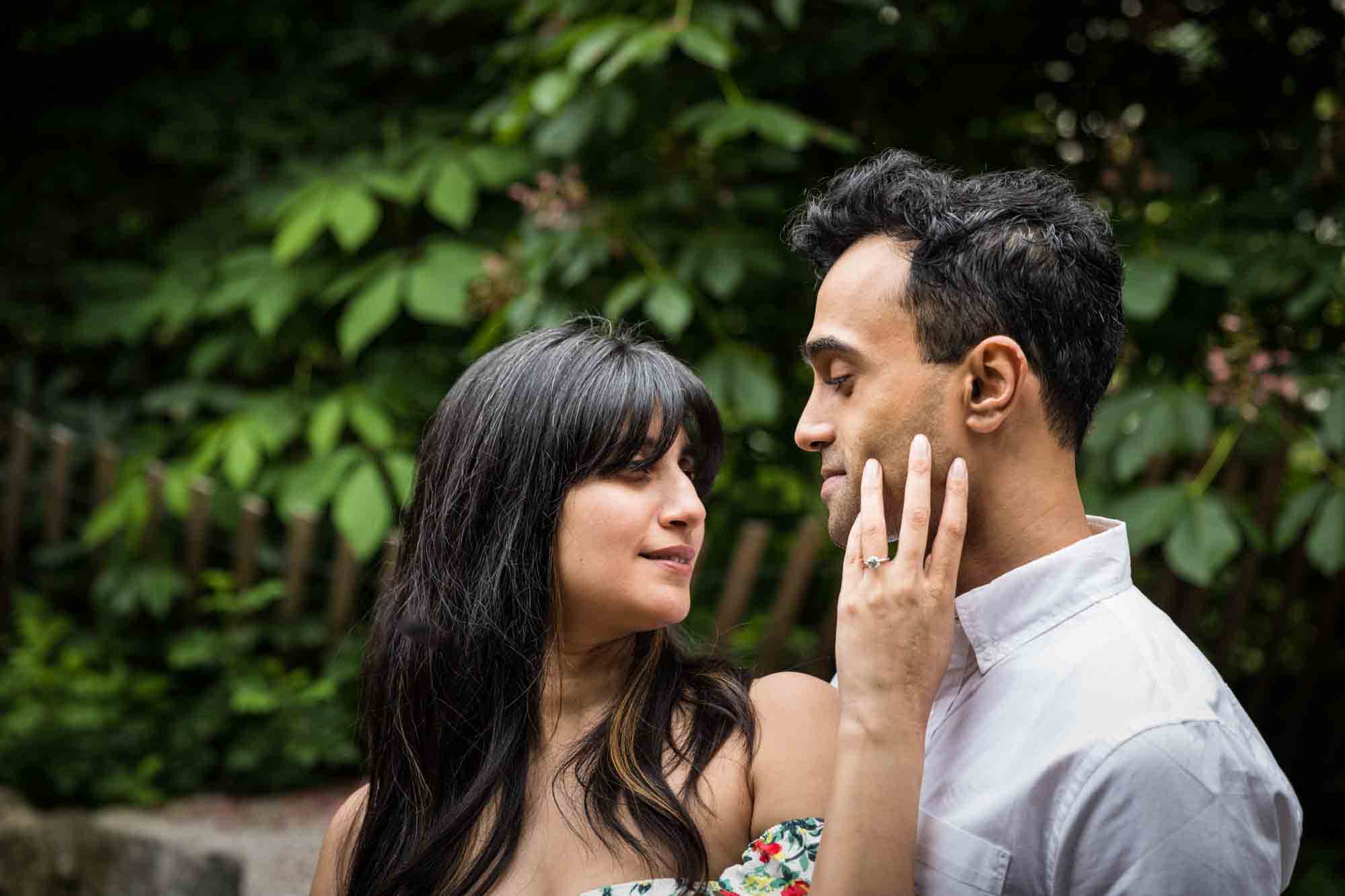 Woman looking back at man and touching his cheek during a Brooklyn Bridge Park engagement photo shoot