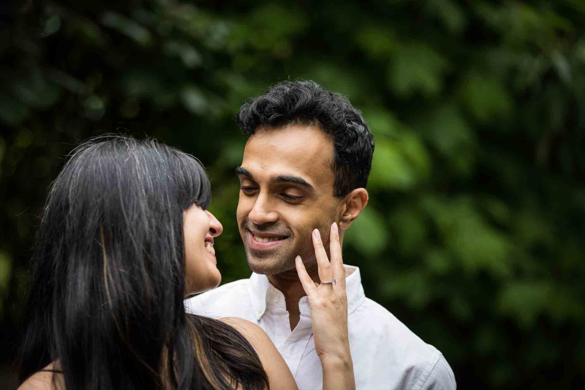 Woman looking back at man and touching his cheek during a Brooklyn Bridge Park engagement photo shoot