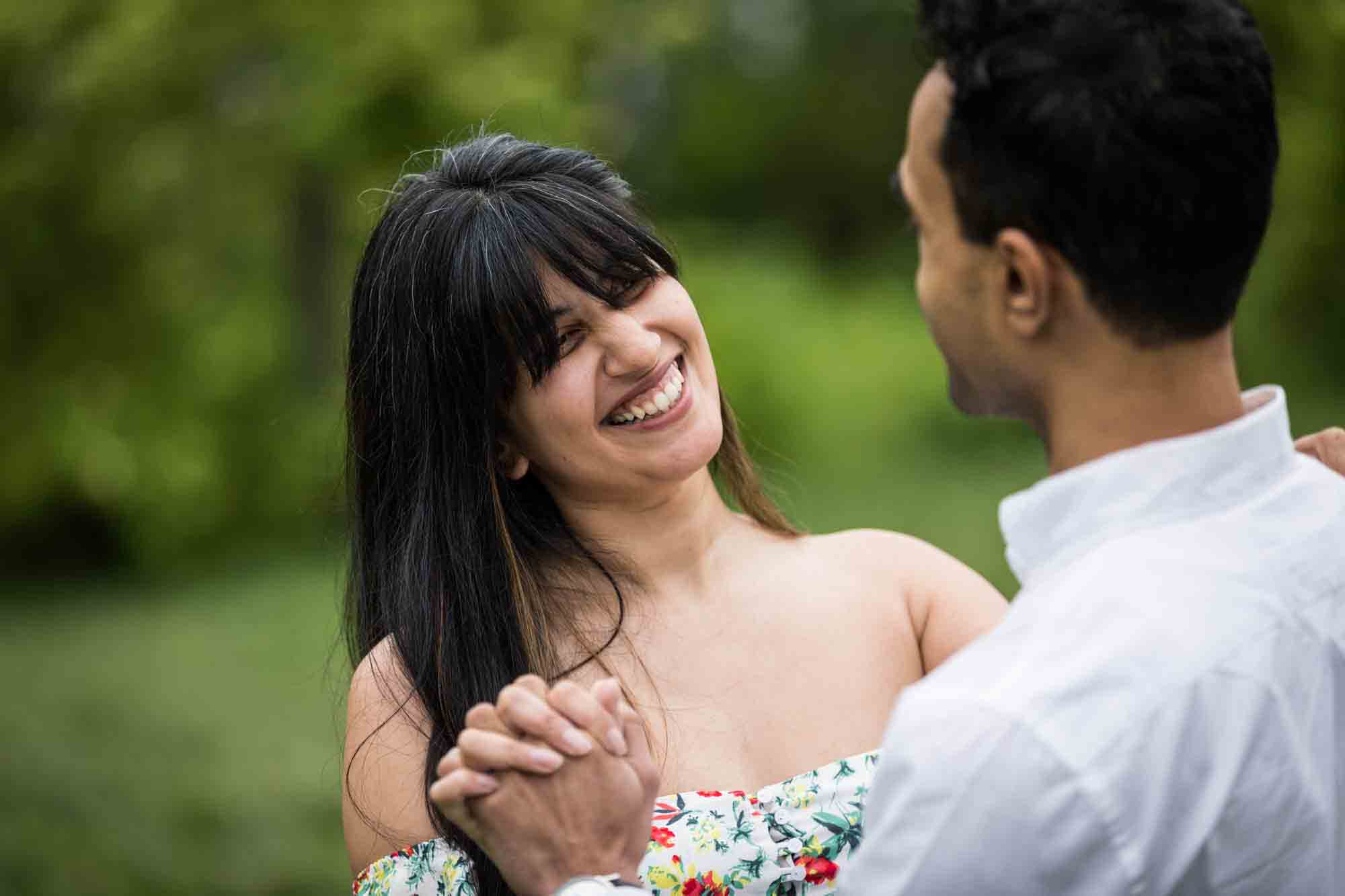 Woman dancing with man in grass during a Brooklyn Bridge Park engagement photo shoot