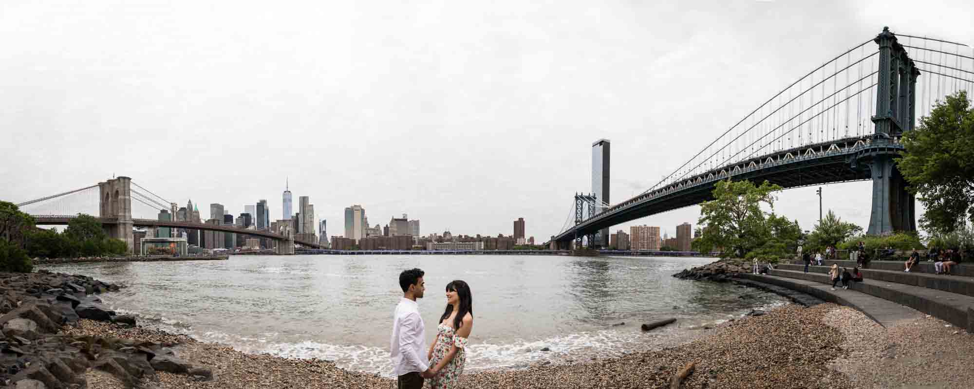 Panorama shot of couple on beach with NYC skyline in background at Brooklyn Bridge Park