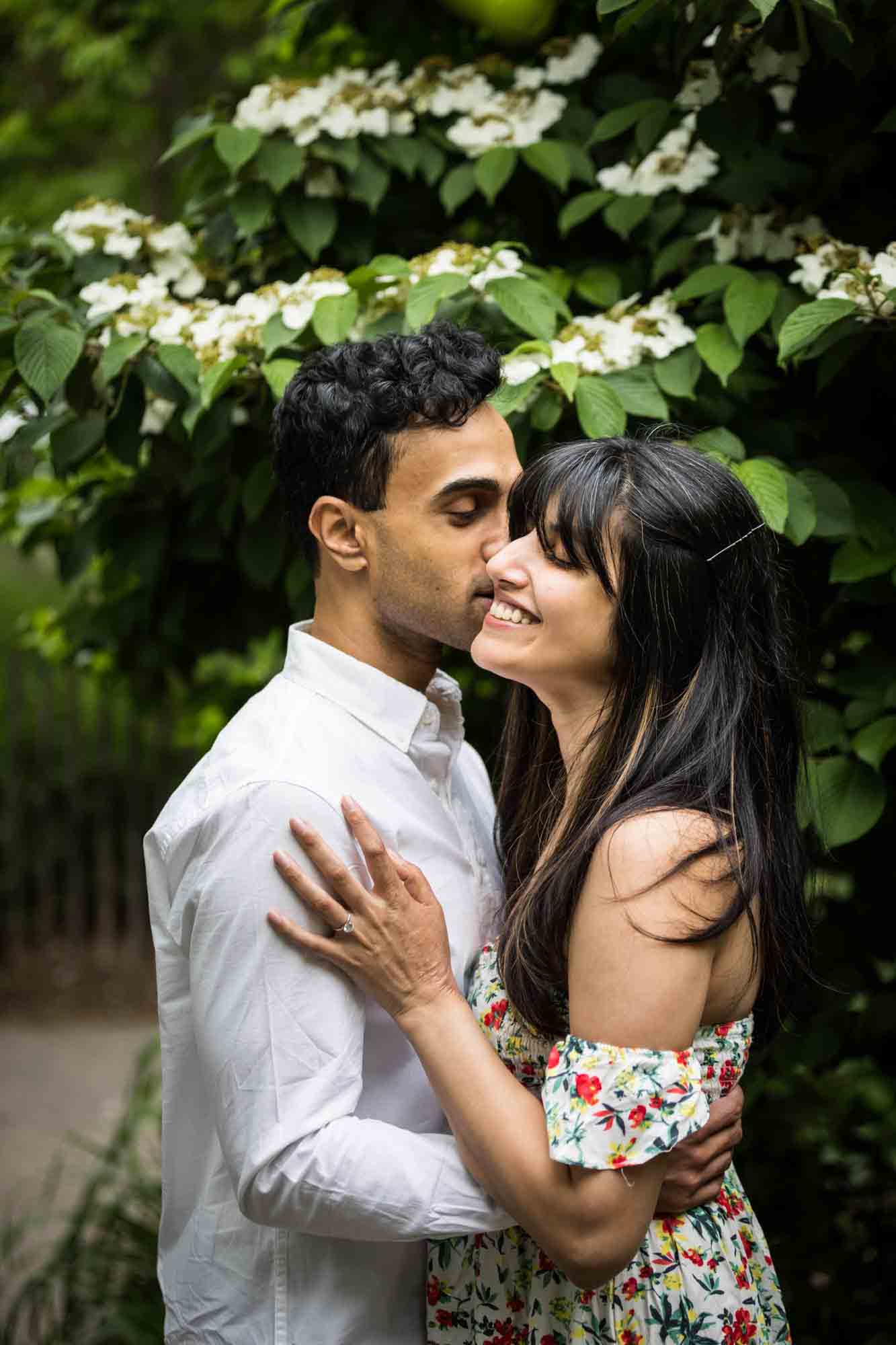 Couple cuddling in front of white hydrangea bush at Brooklyn Bridge Park