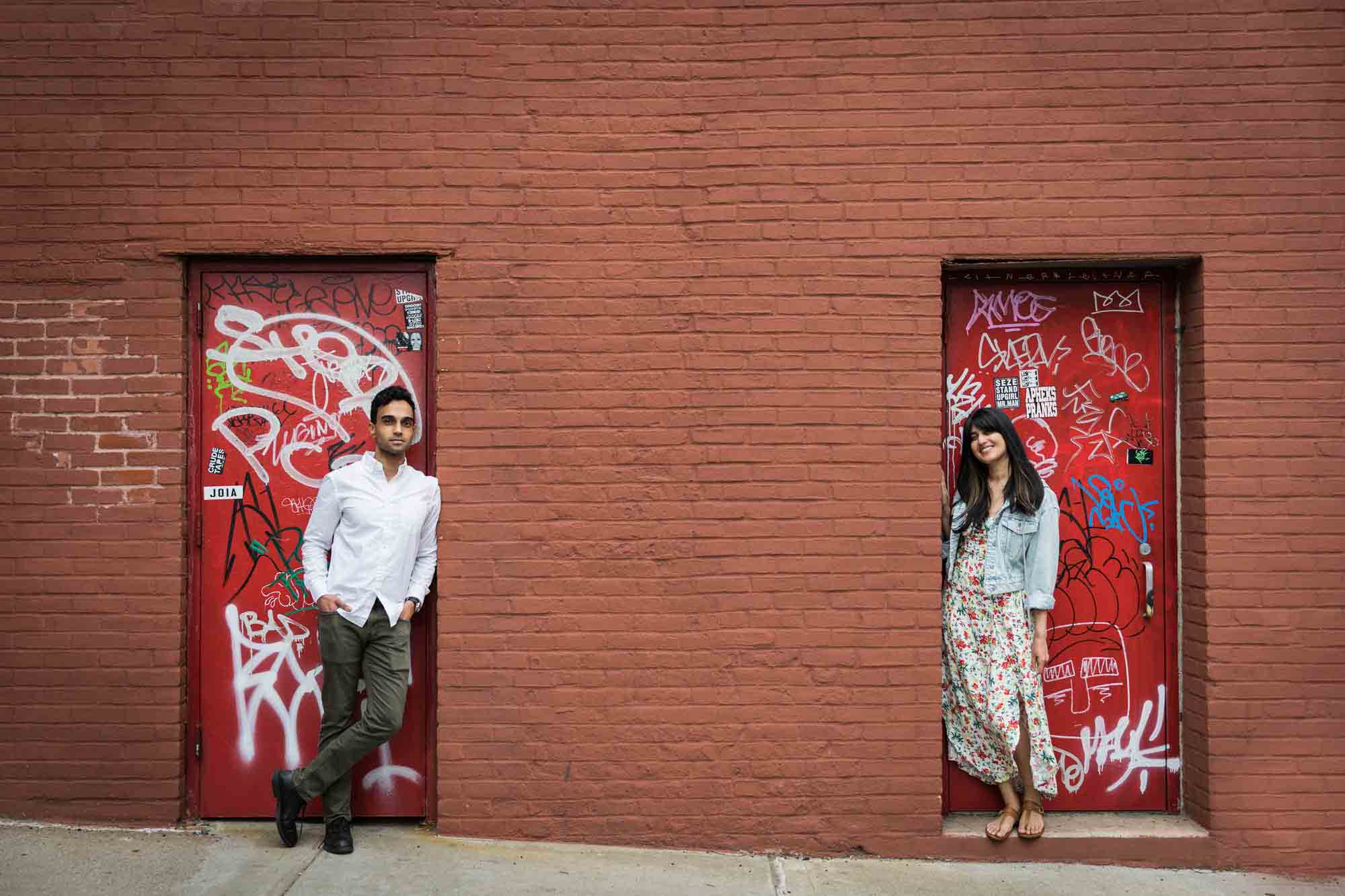 Couple standing in front of red doors covered with graffiti during a Brooklyn Bridge Park engagement photo shoot