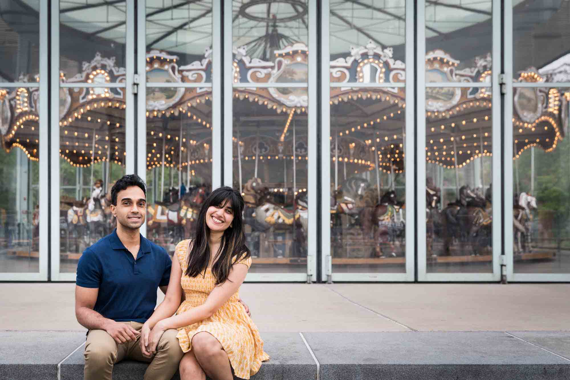 Couple sitting in front of Jane's Carousel during a Brooklyn Bridge Park engagement photo shoot