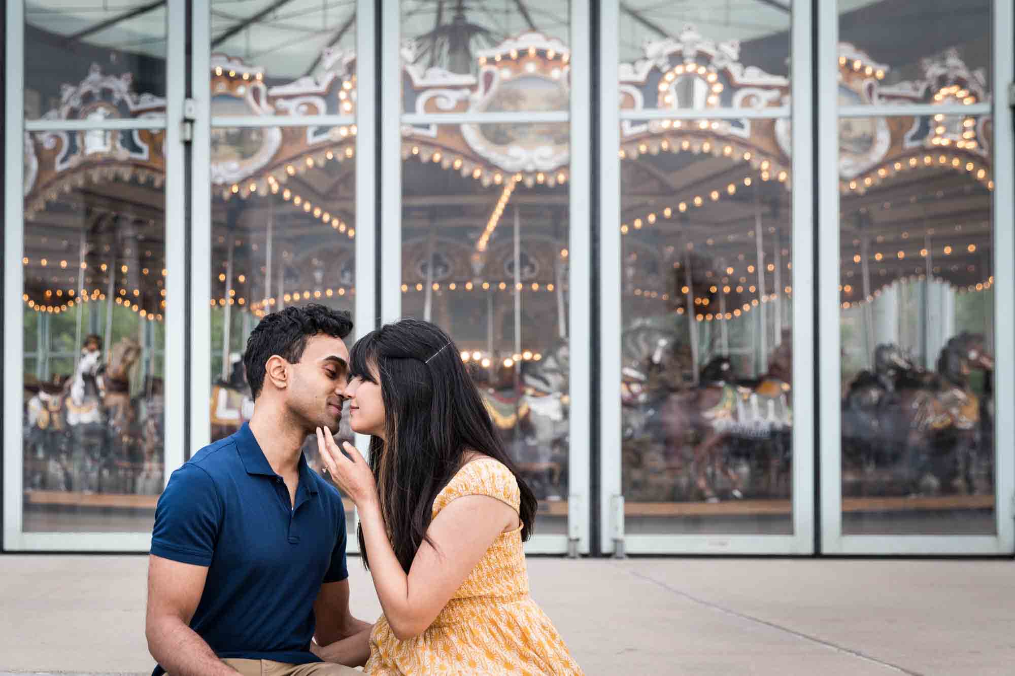 Couple kissing in front of Jane's Carousel during a Brooklyn Bridge Park engagement photo shoot
