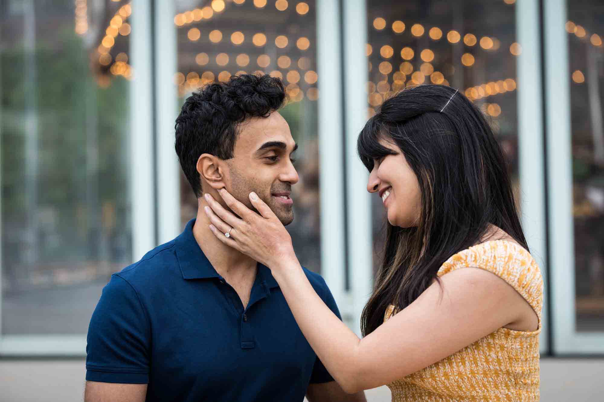 Woman touching man on the cheek during a Brooklyn Bridge Park engagement photo shoot