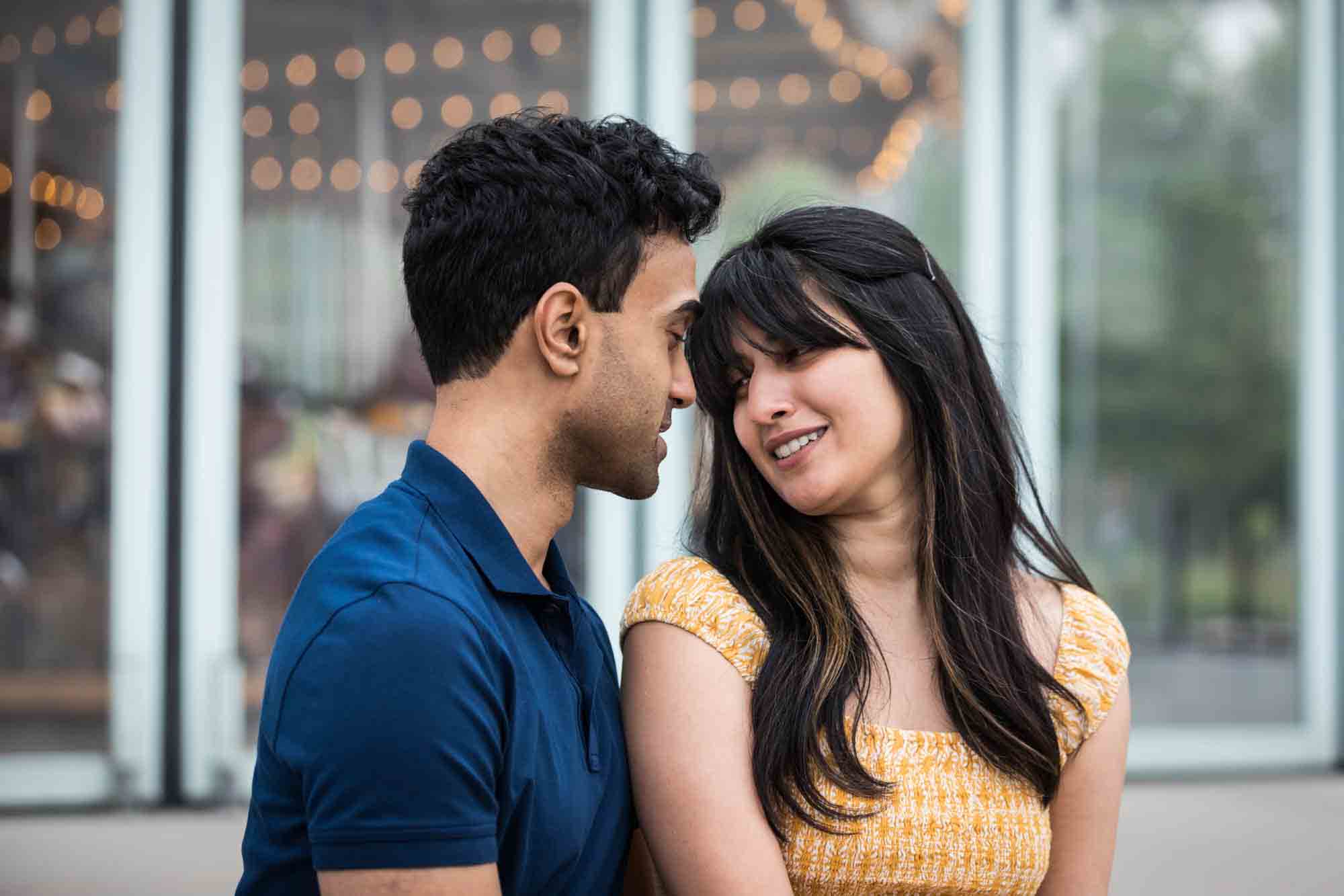 Couple sitting in front of Jane's Carousel during a Brooklyn Bridge Park engagement photo shoot