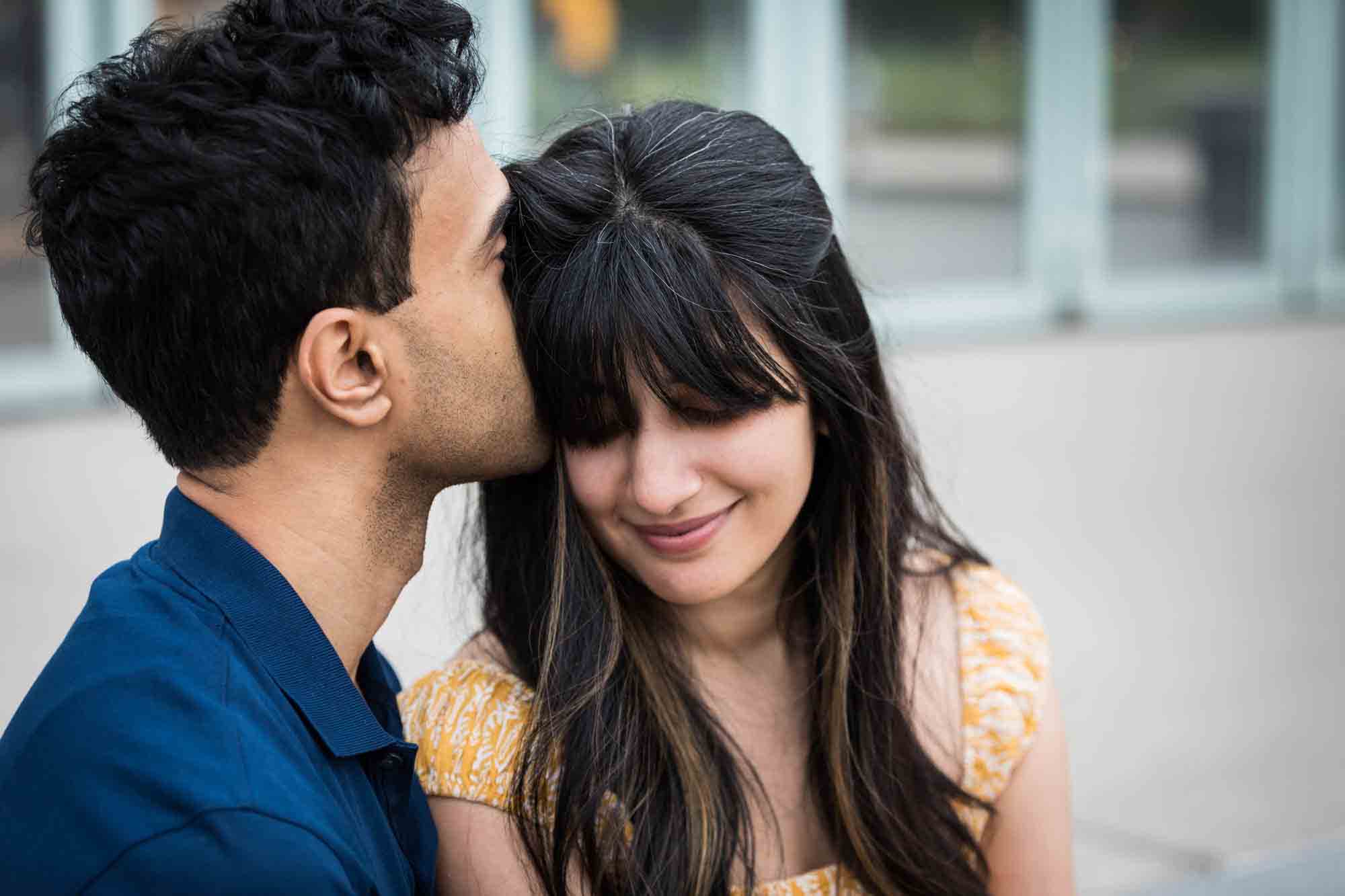 Man kissing woman on the side of the head during a Brooklyn Bridge Park engagement photo shoot