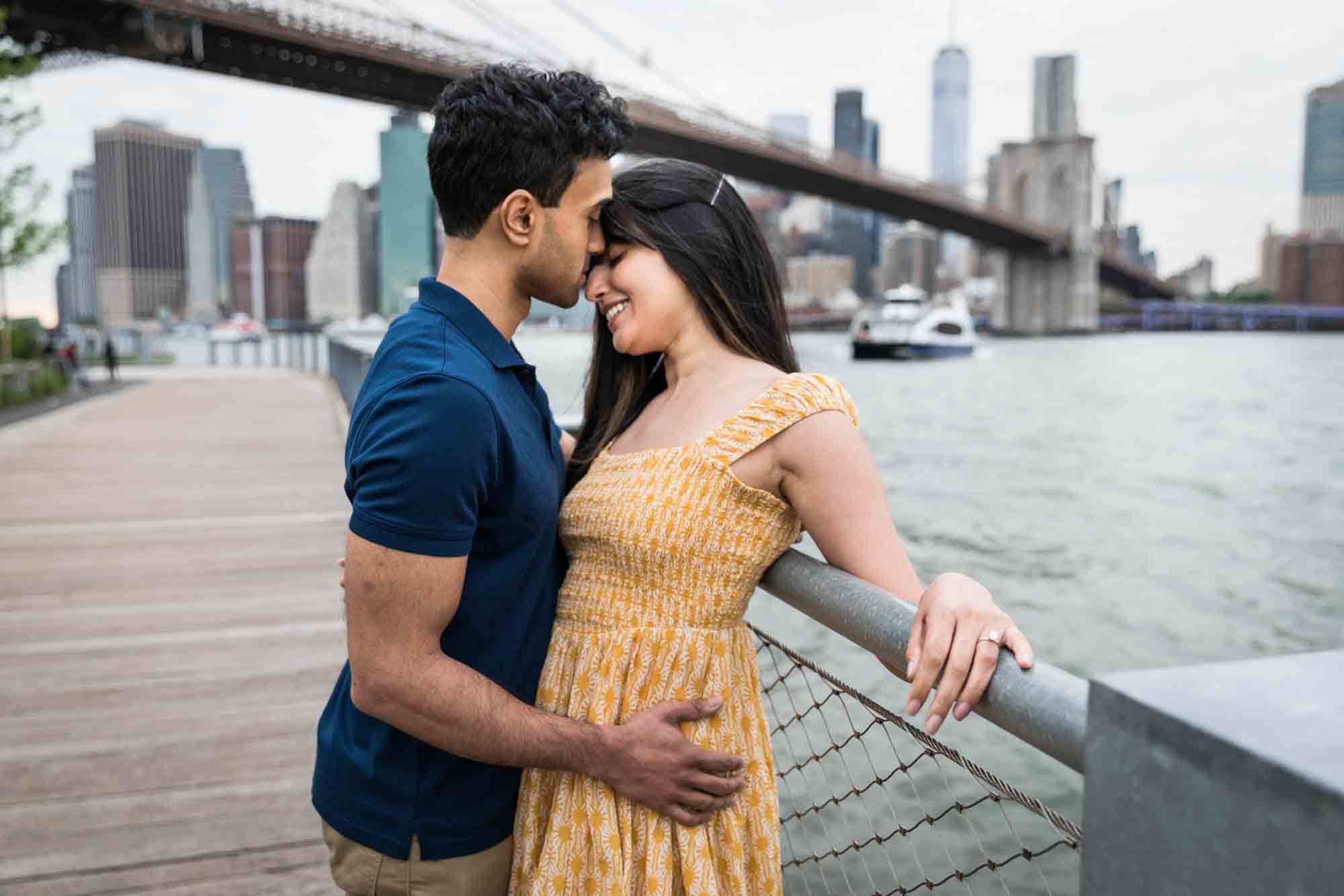 Couple cuddling along railing on boardwalk at Brooklyn Bridge Park