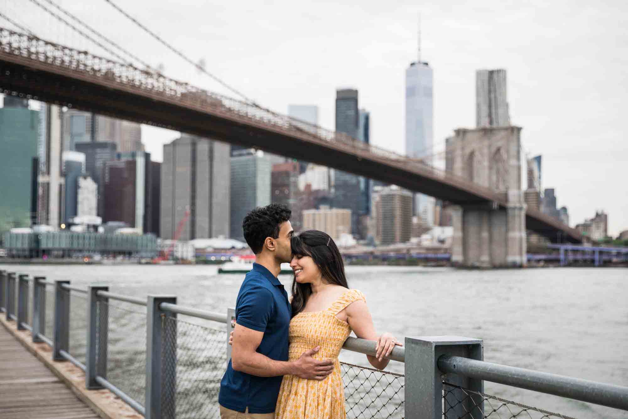 Couple cuddling along railing on boardwalk at Brooklyn Bridge Park