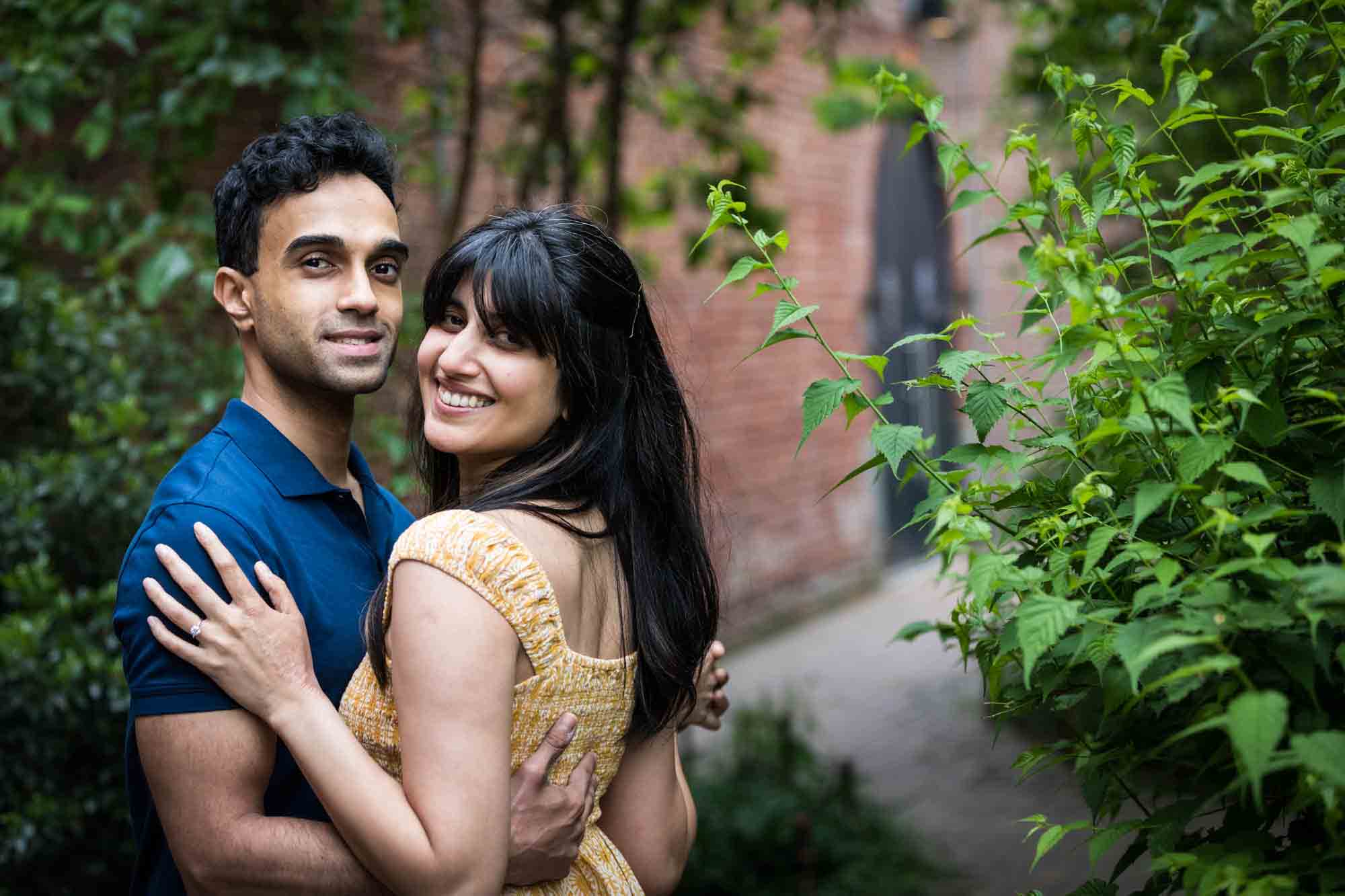 Couple looking over shoulder in walled garden during a Brooklyn Bridge Park engagement photo shoot