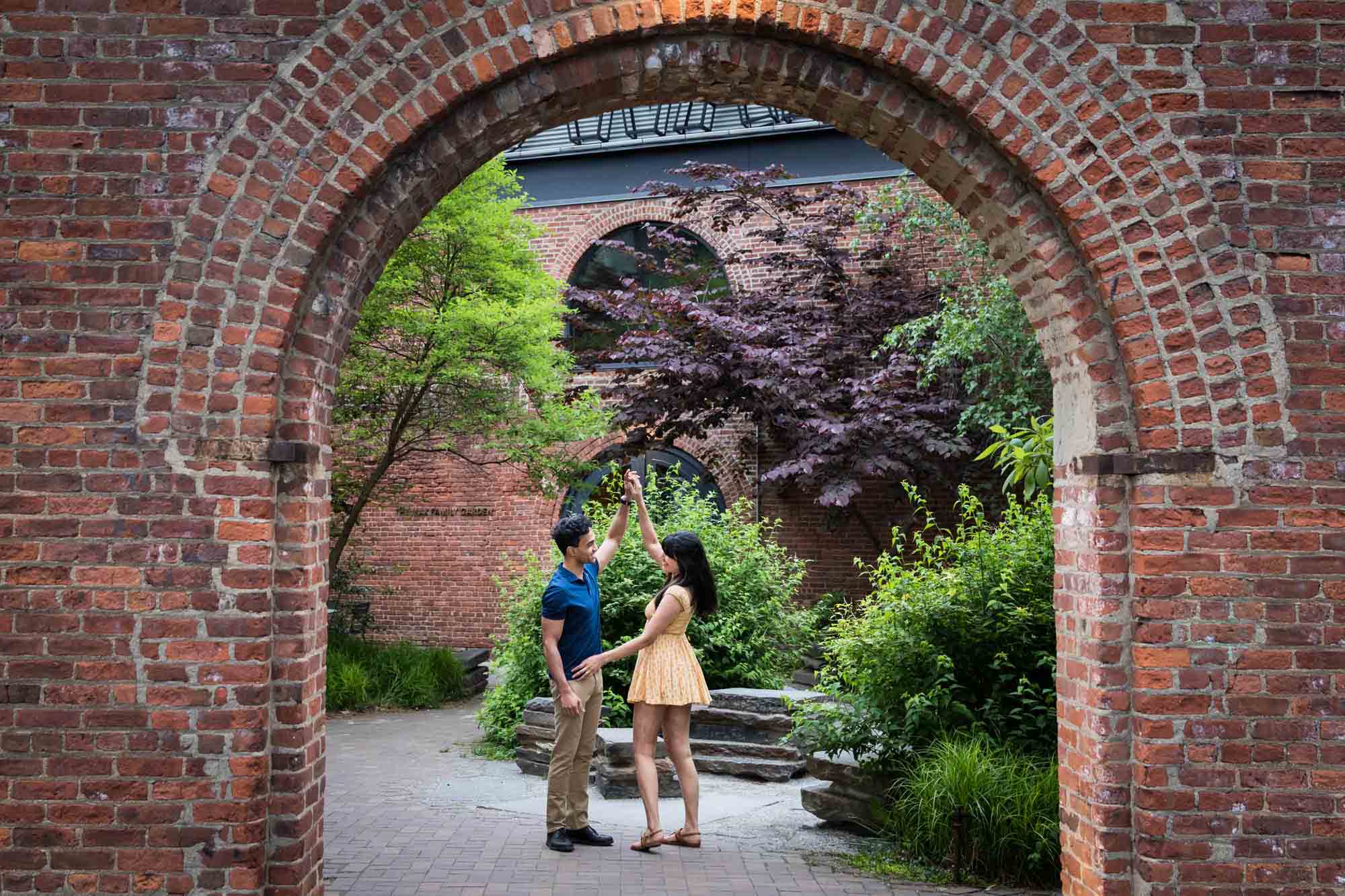 Couple dancing in archway in walled garden during a Brooklyn Bridge Park engagement photo shoot