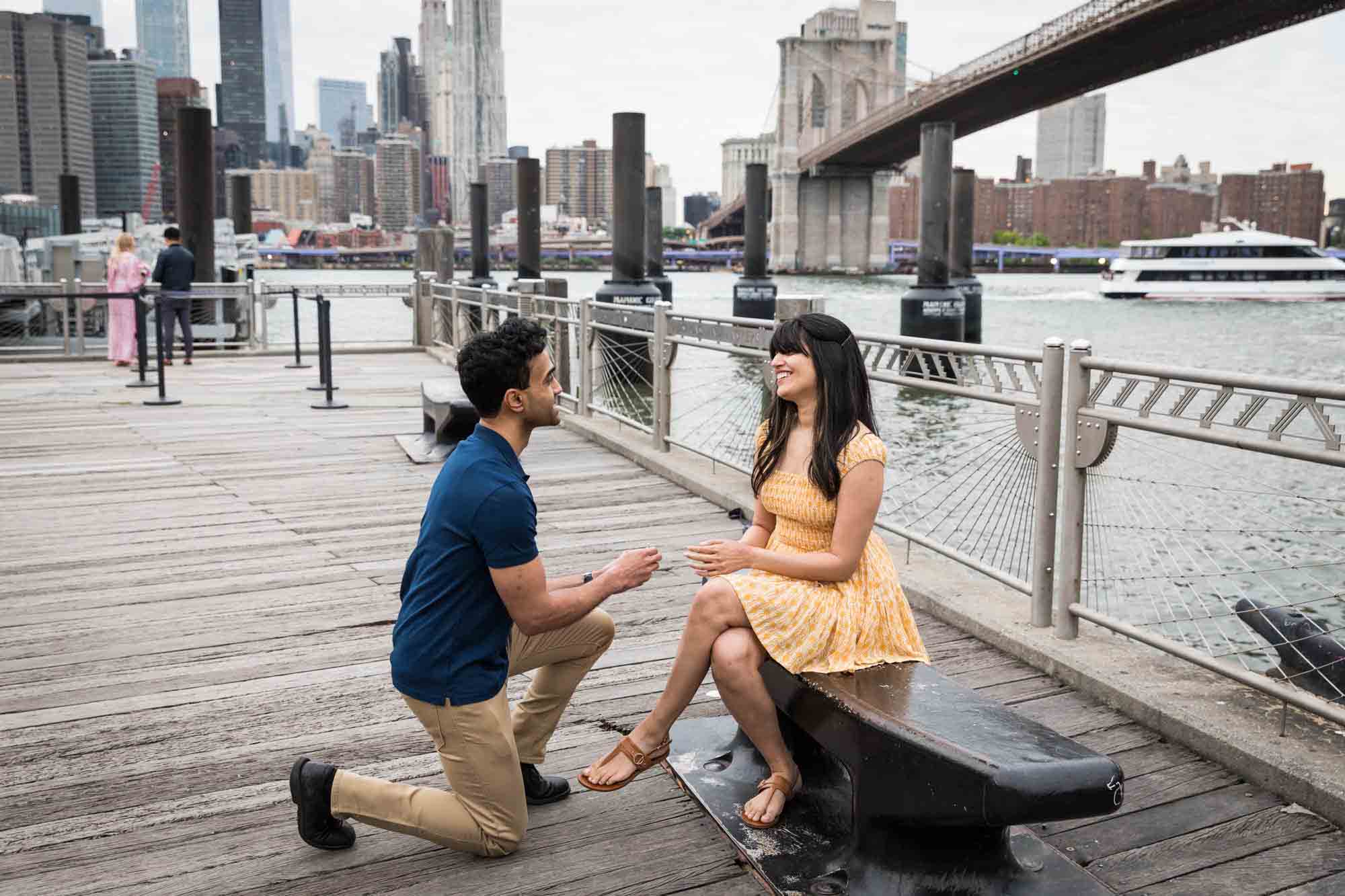 Man proposing to woman on a bench on a dock in Brooklyn Bridge Park