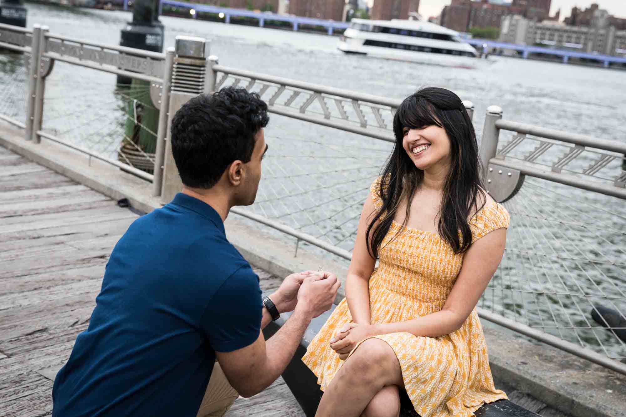 Man proposing to woman on a bench on a dock in Brooklyn Bridge Park